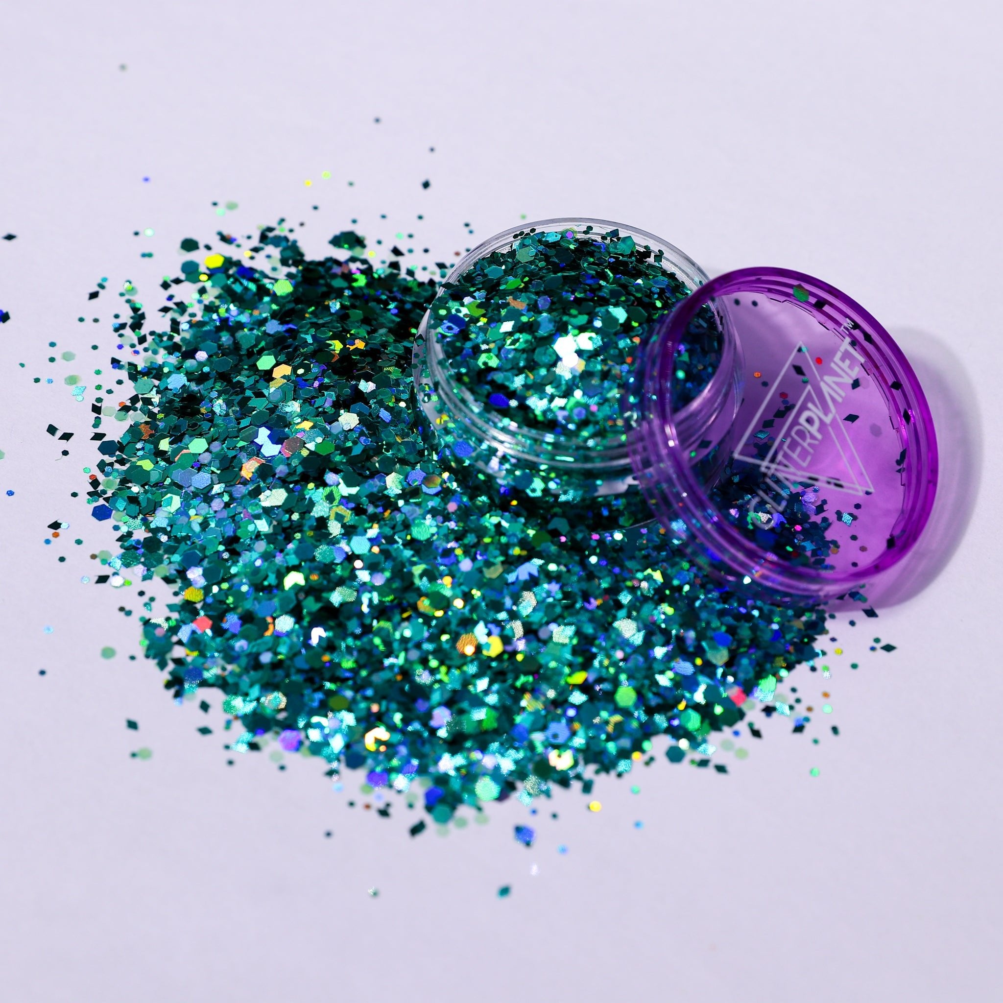 Turquoise glitter spilling out of a purple container on a light gray background