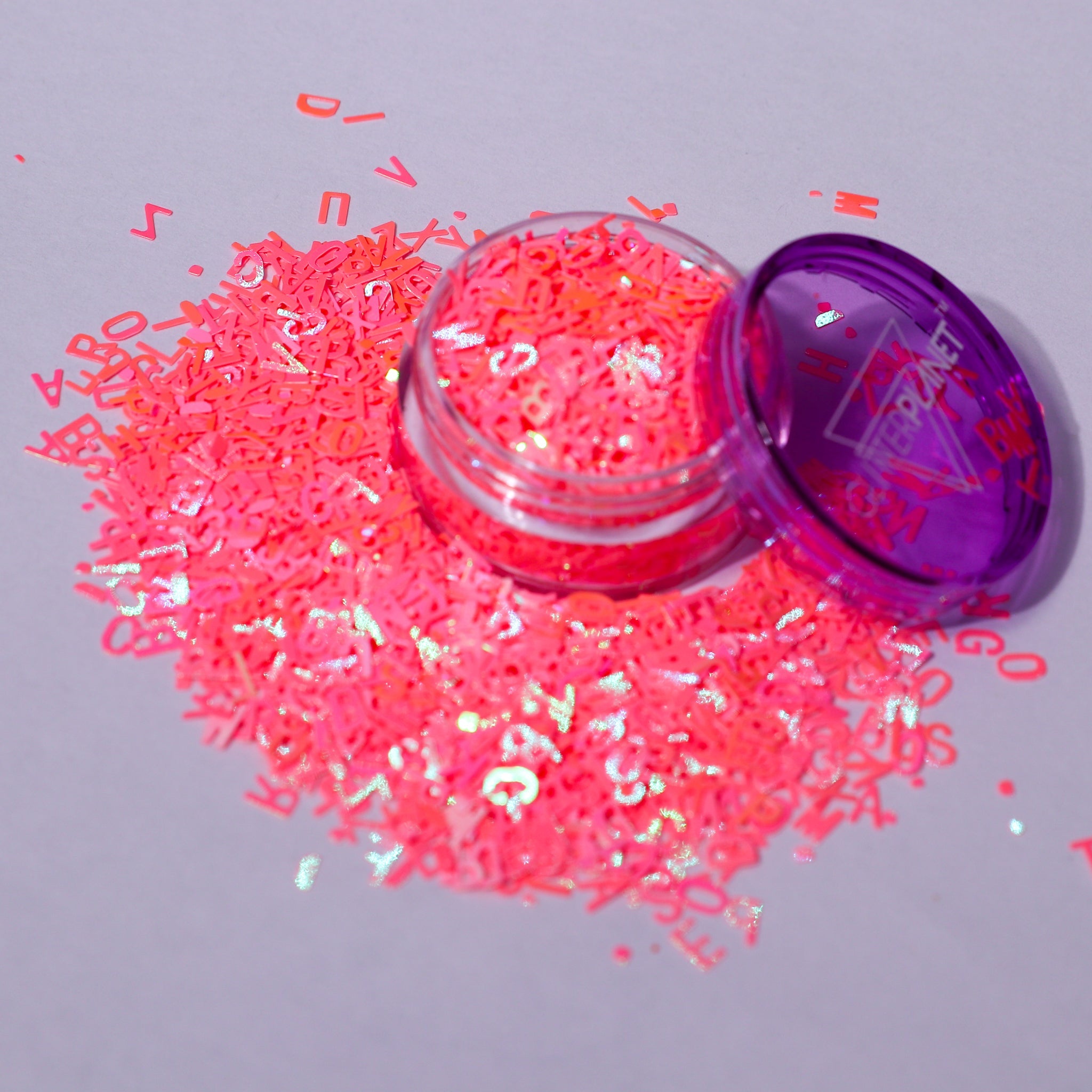coral glitter with letters and numbers spilling out of a purple container on a gray background