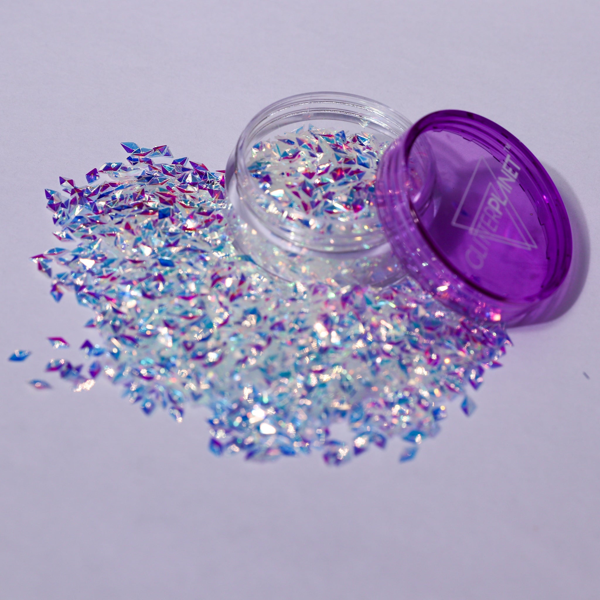 Iridescent glitter spilling out of a purple container on a light gray background