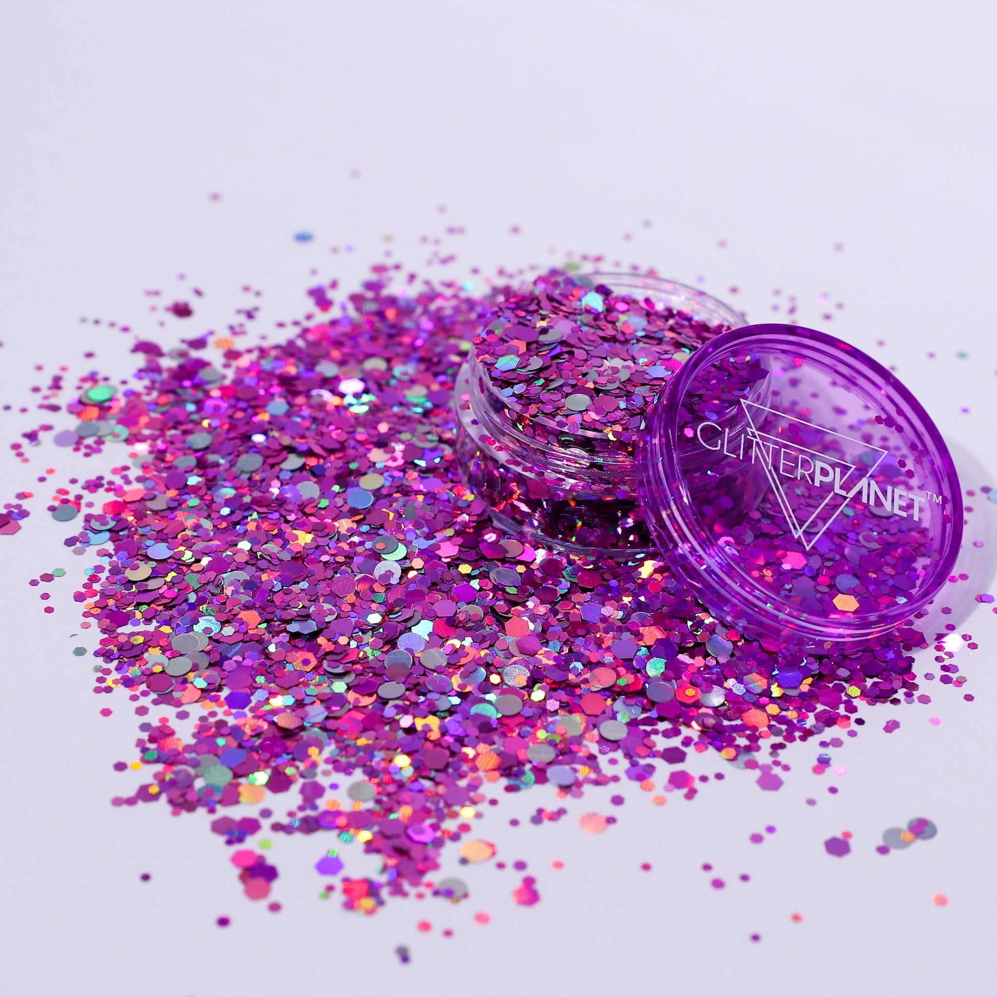 Purple glitter container with scattered glitter on a light purple background