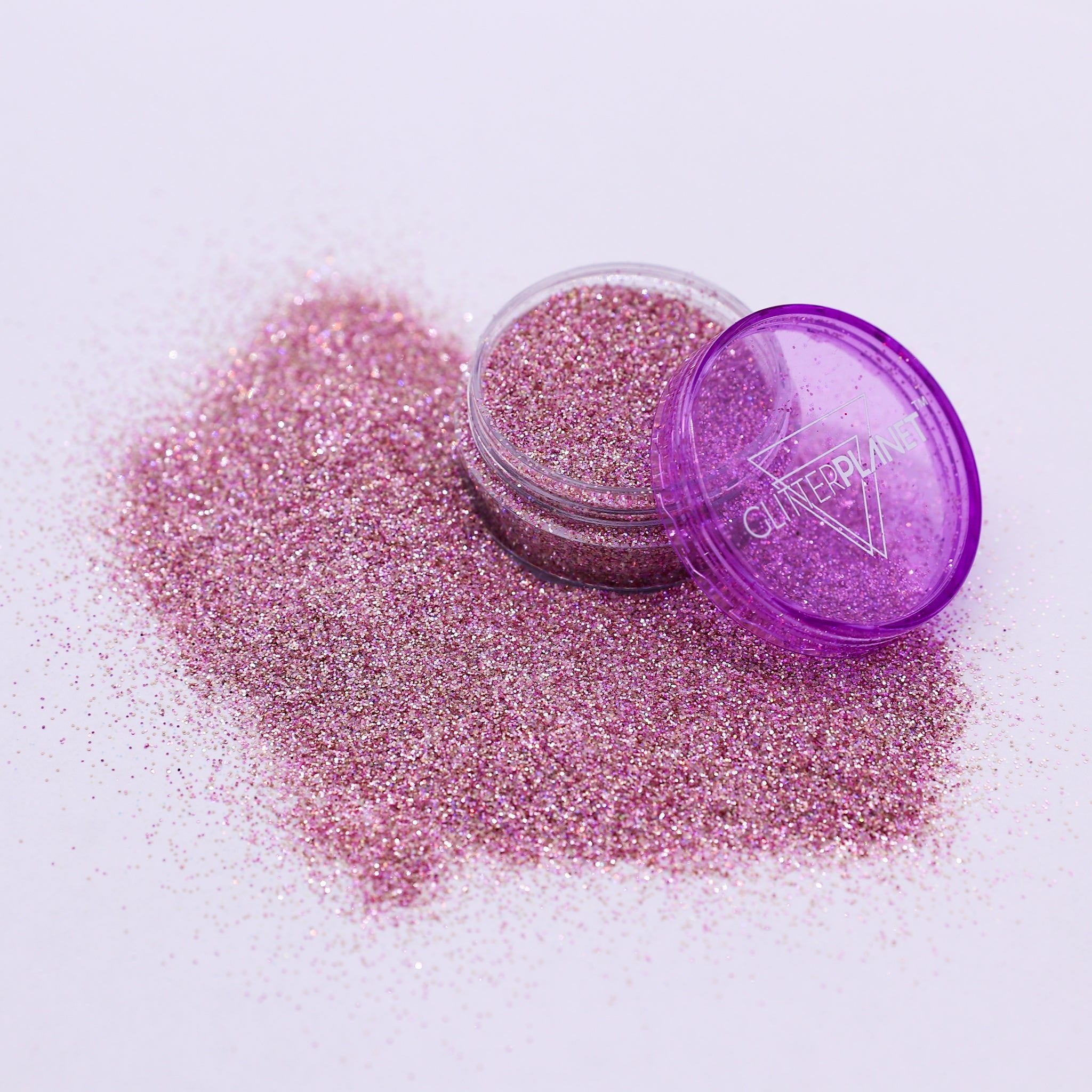 Pink glitter in an open container with a purple lid on a white background