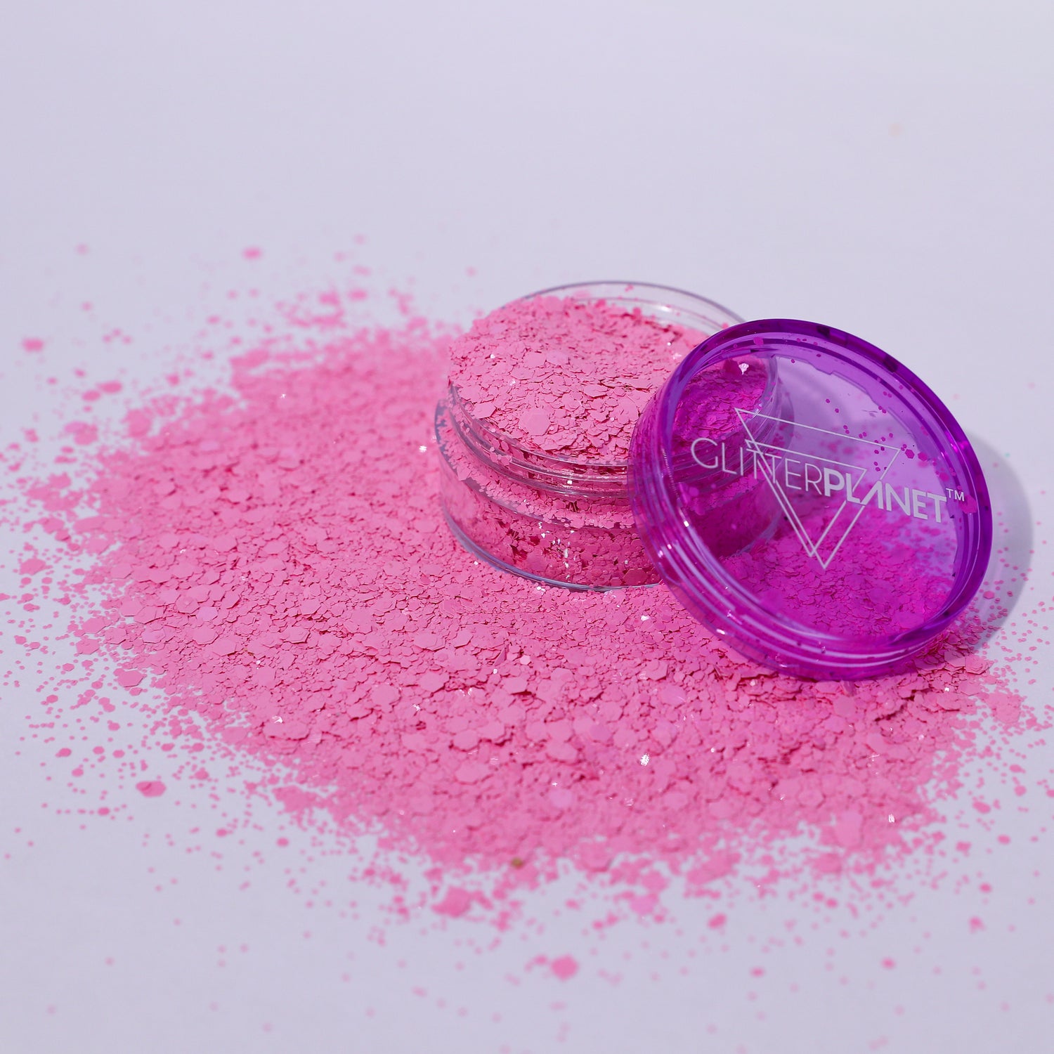 Pink glitter powder with a purple container on a white background