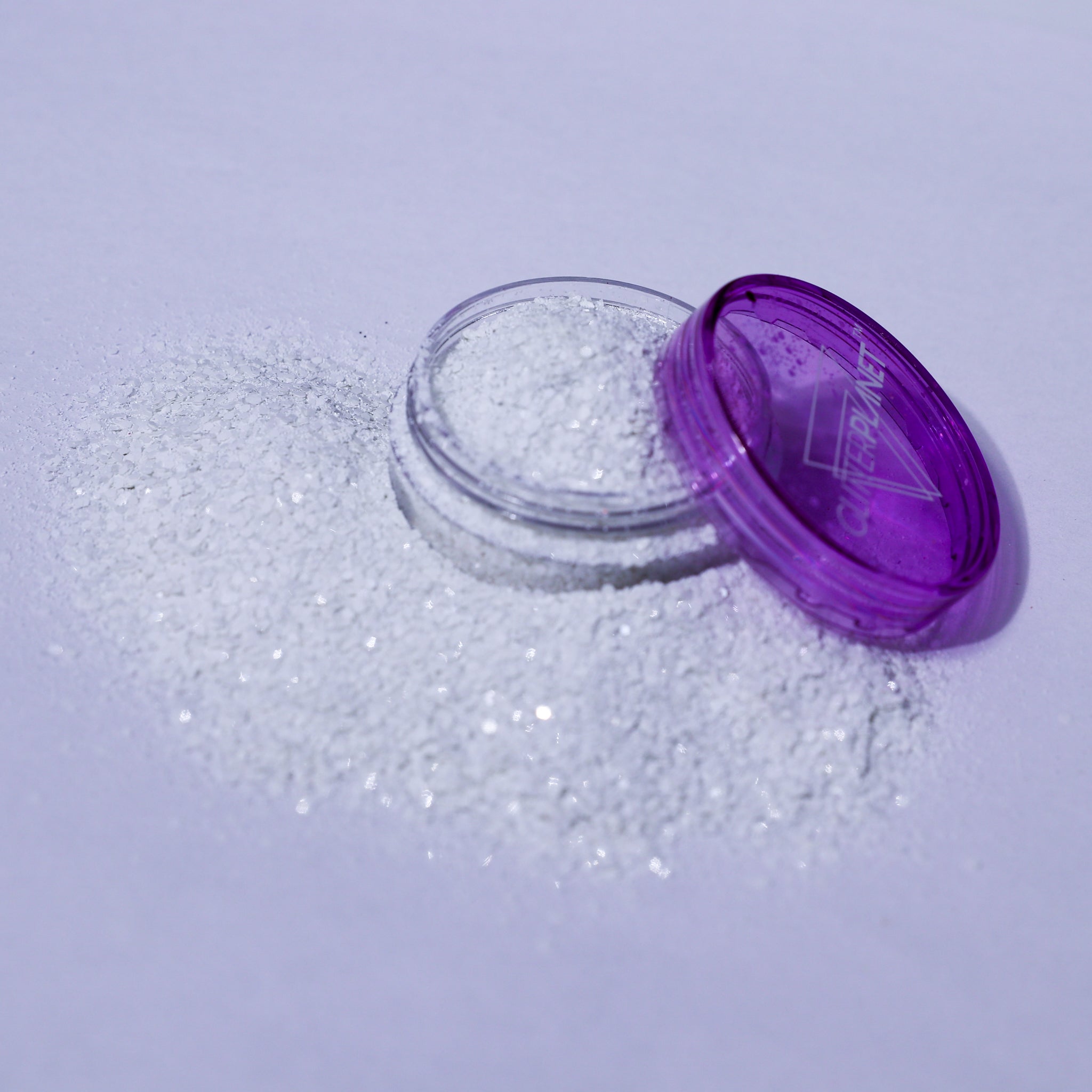 Open container of glitter with purple lid on a light purple background