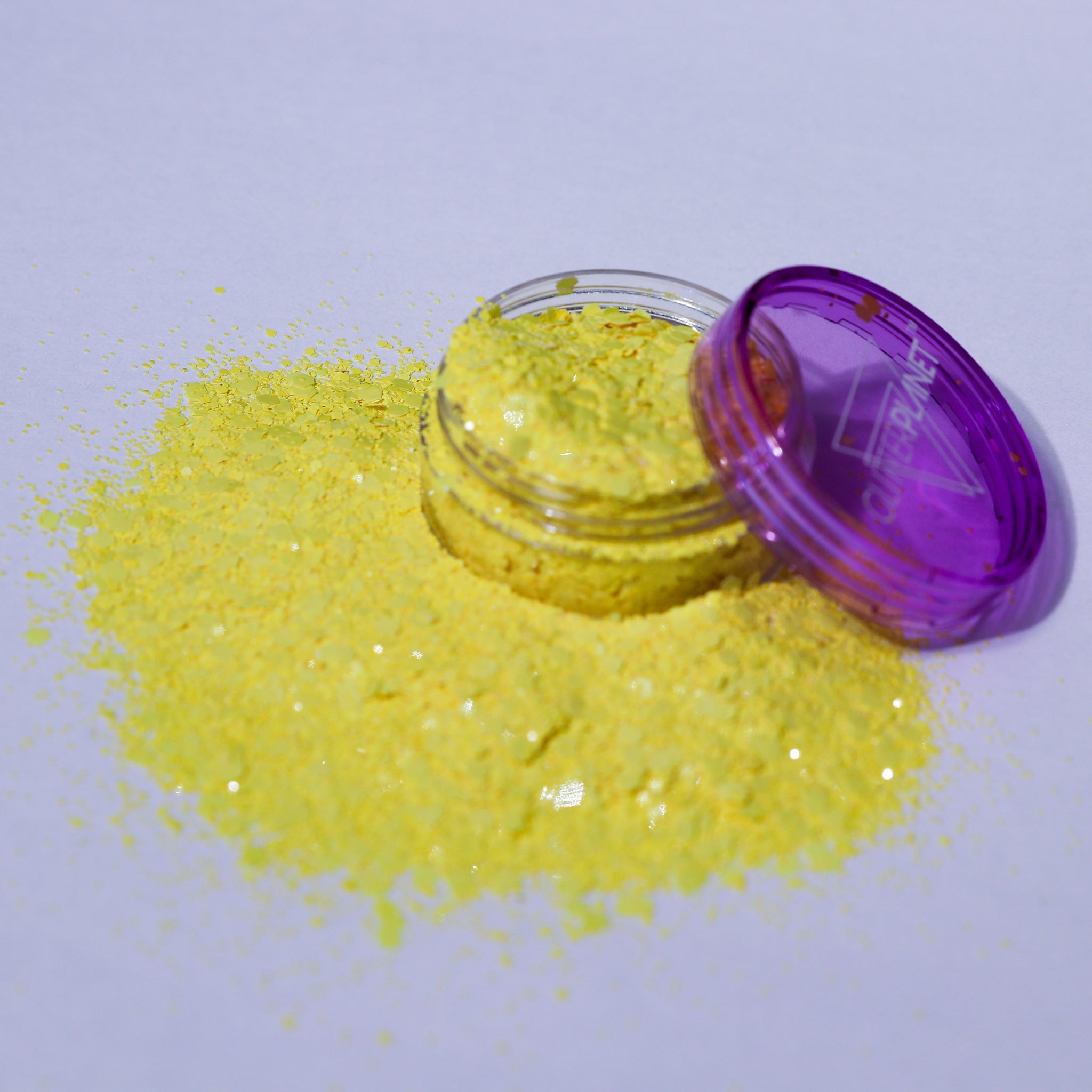 Yellow glitter in an open jar with a purple lid on a light purple background