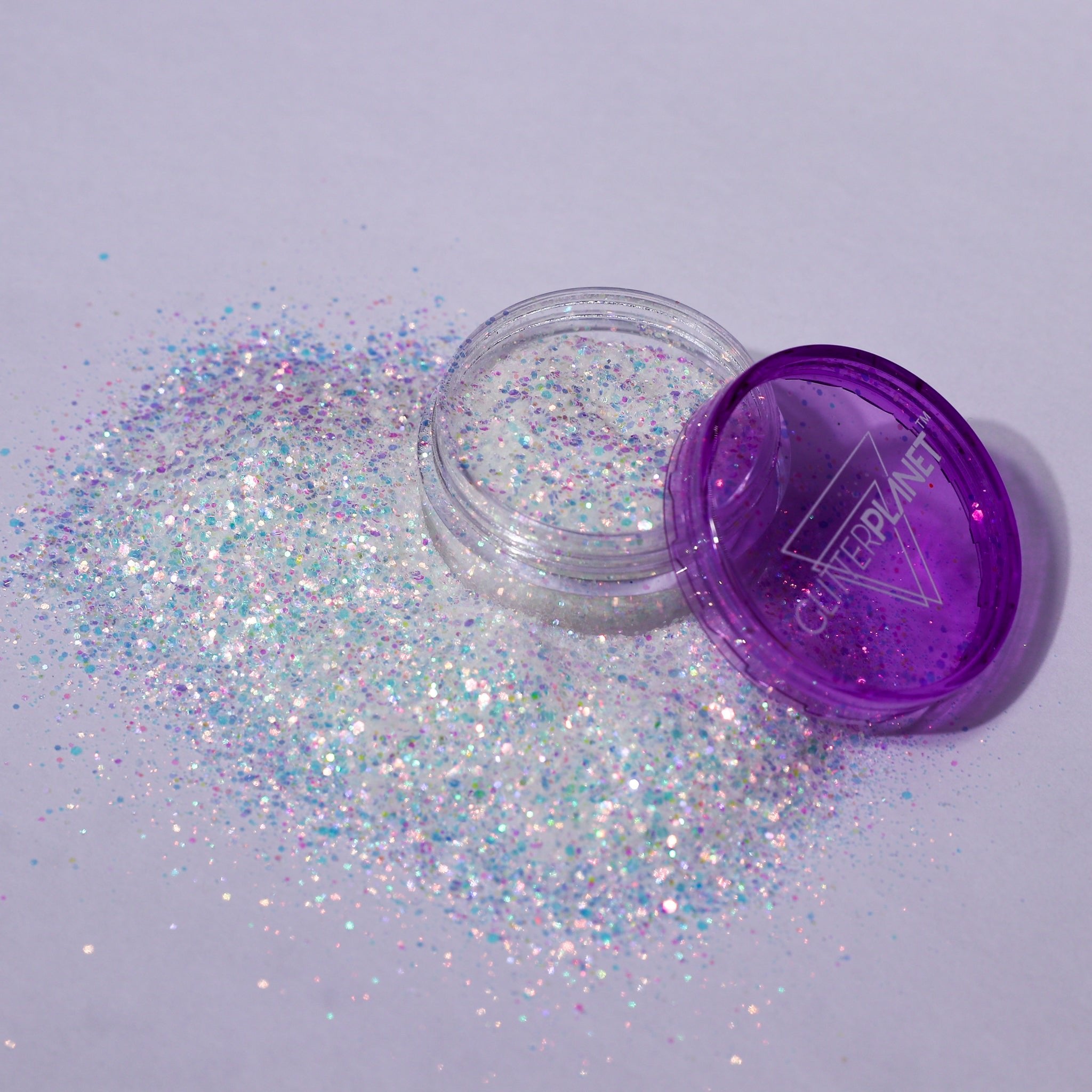 Open container of glitter with purple lid on a light gray background