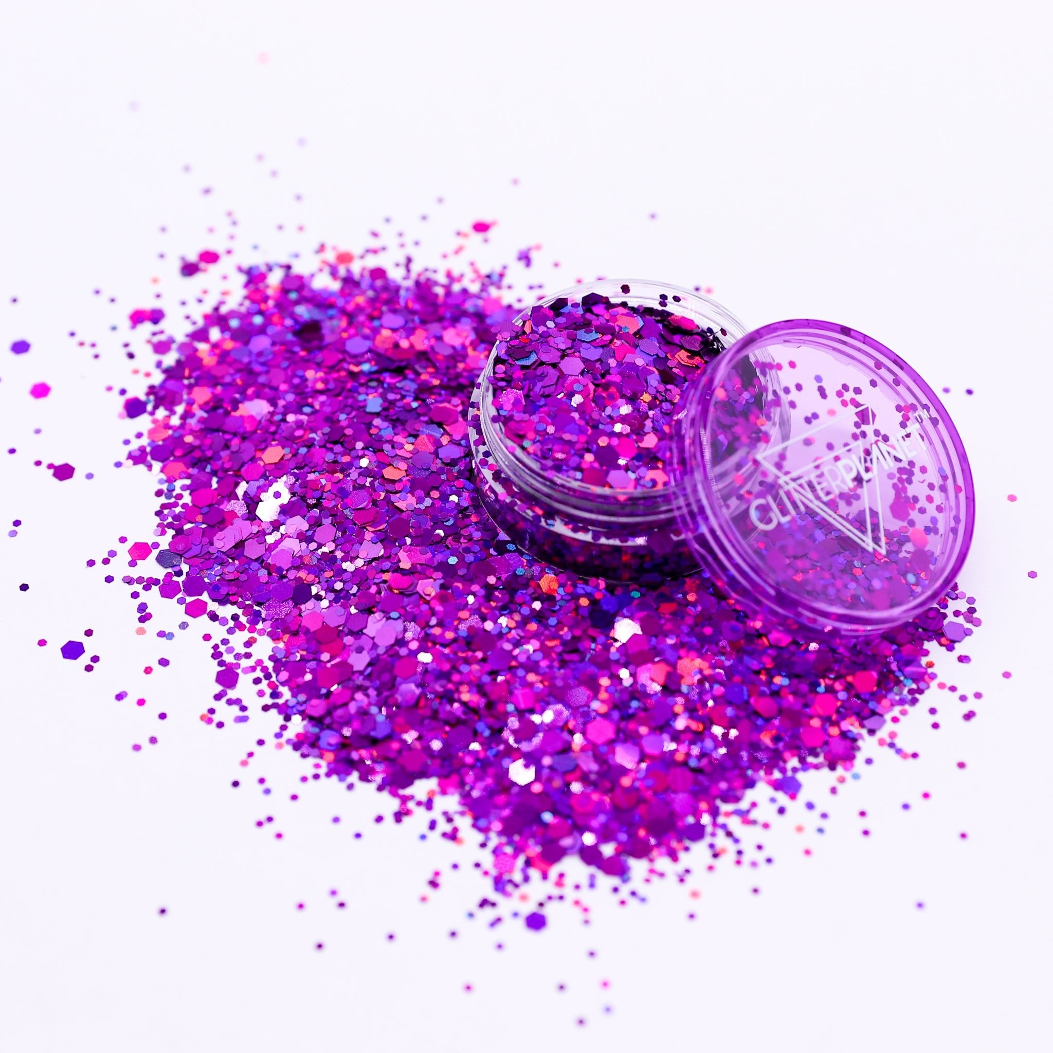 Open container of purple glitter with spilled glitter on a white background