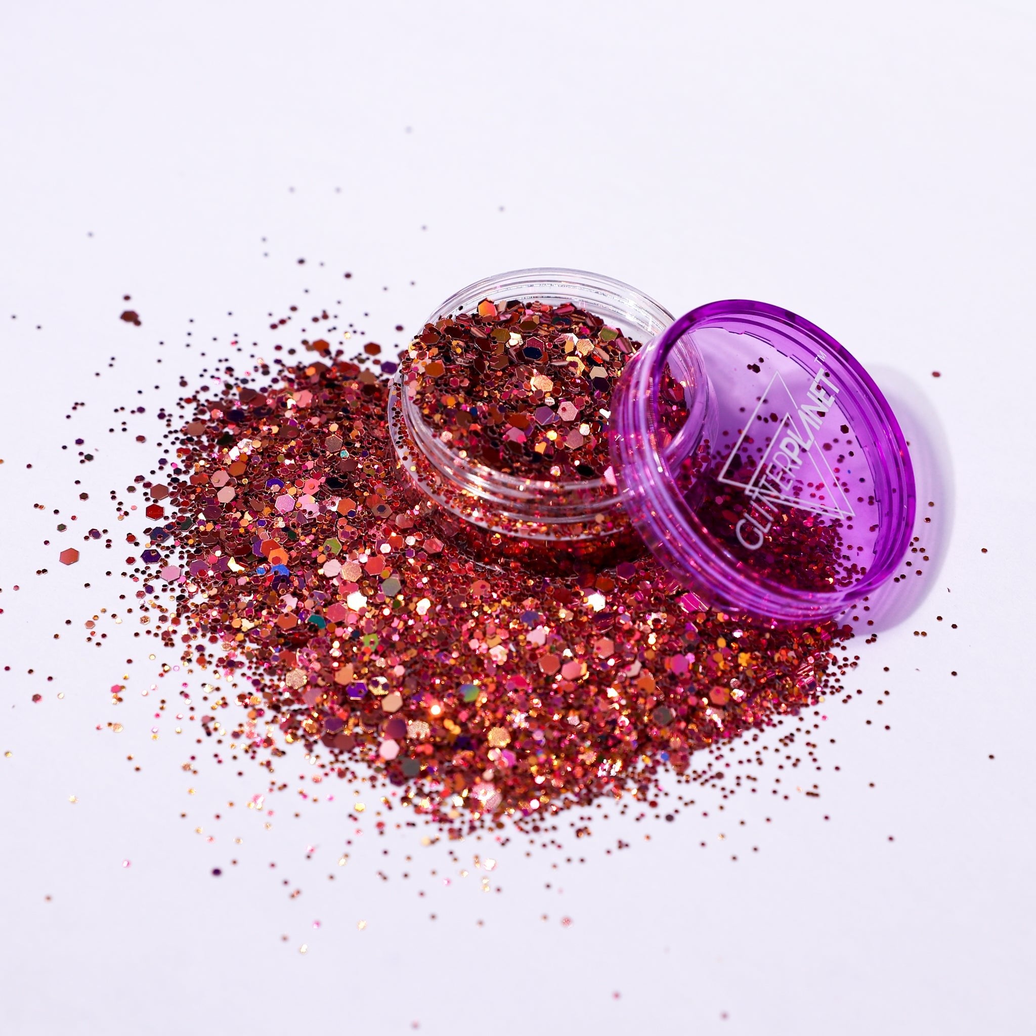 rose gold glitter spilling out of a purple container on a white background