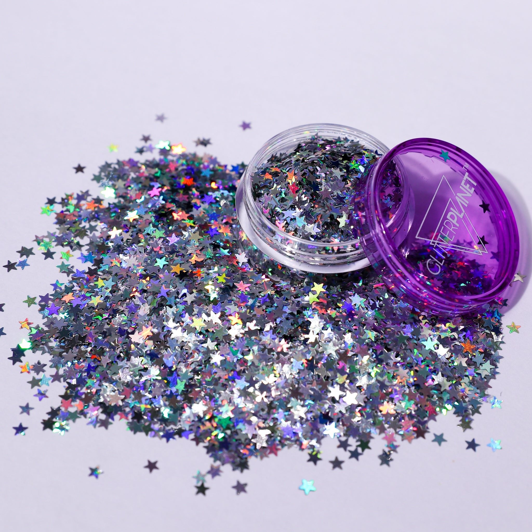 Star-shaped glitter spilling out of a purple container on a light gray background