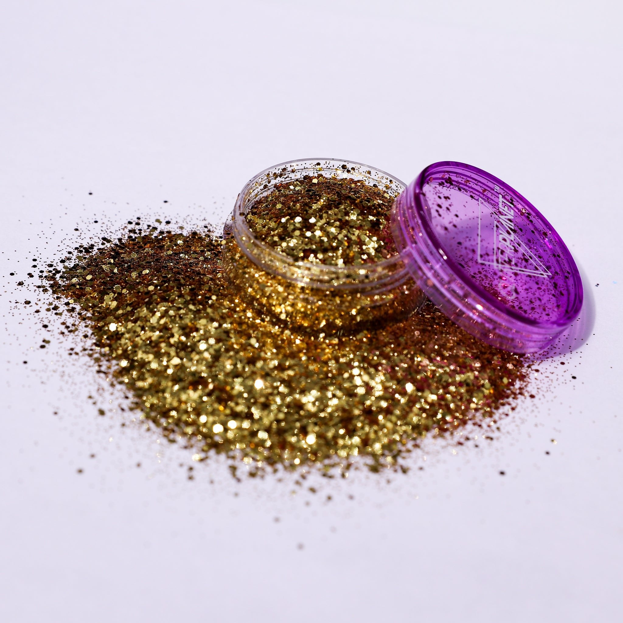 Gold glitter spilling out of a purple container on a white background