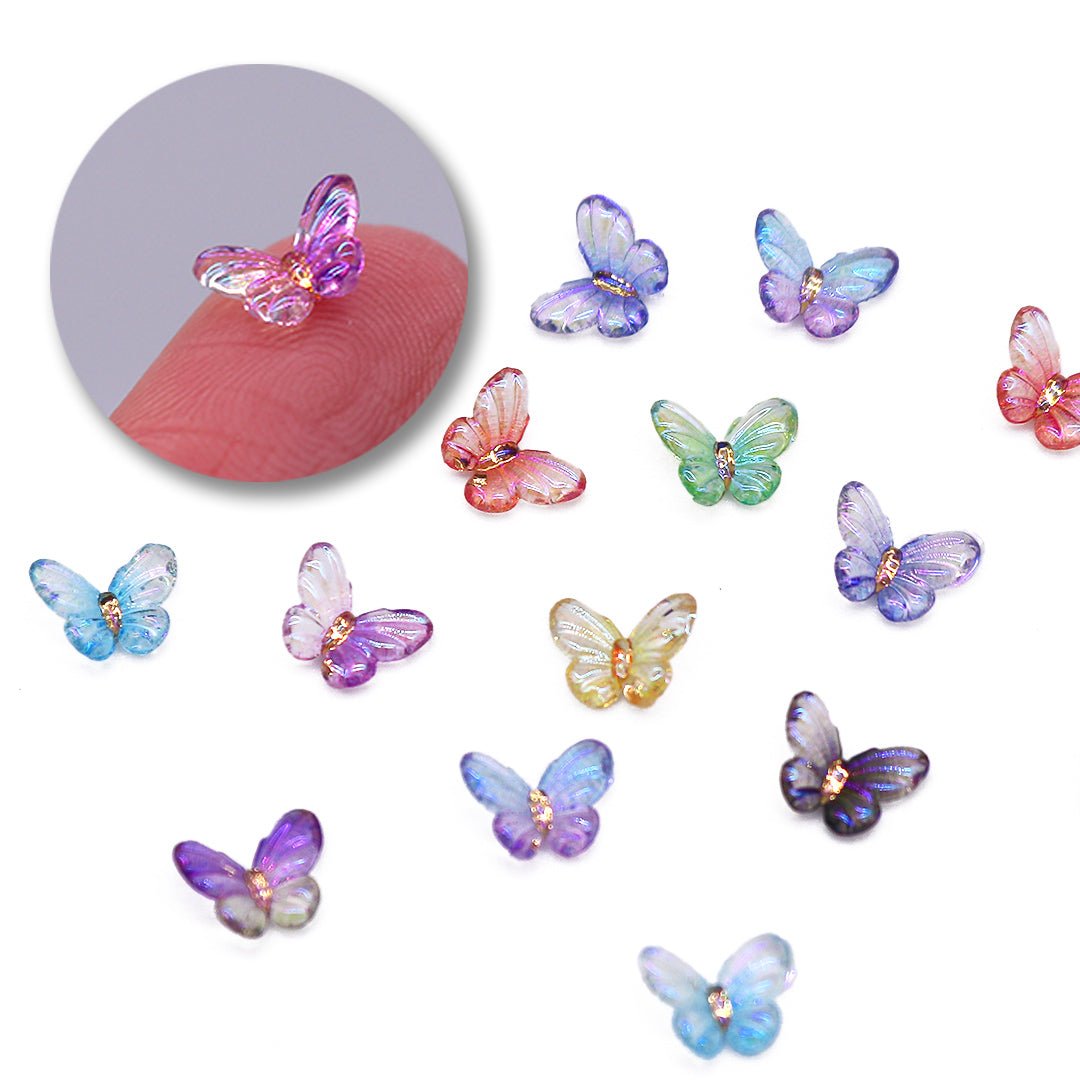 A collection of colorful mini butterfly nail art charms placed on a white surface, with a close-up inset of a single charm on a person&