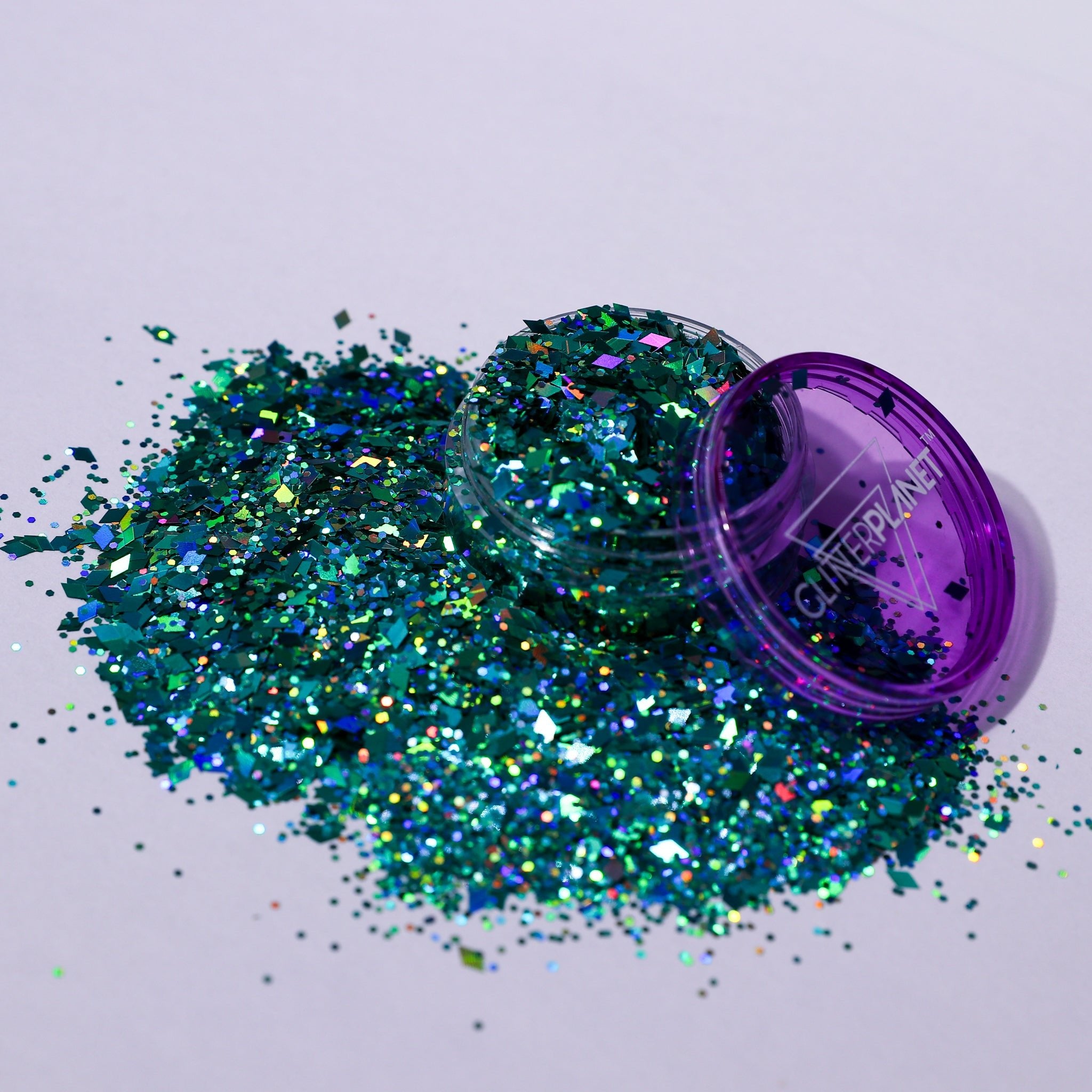 Turquoise glitter spilling out of a purple container on a light gray background