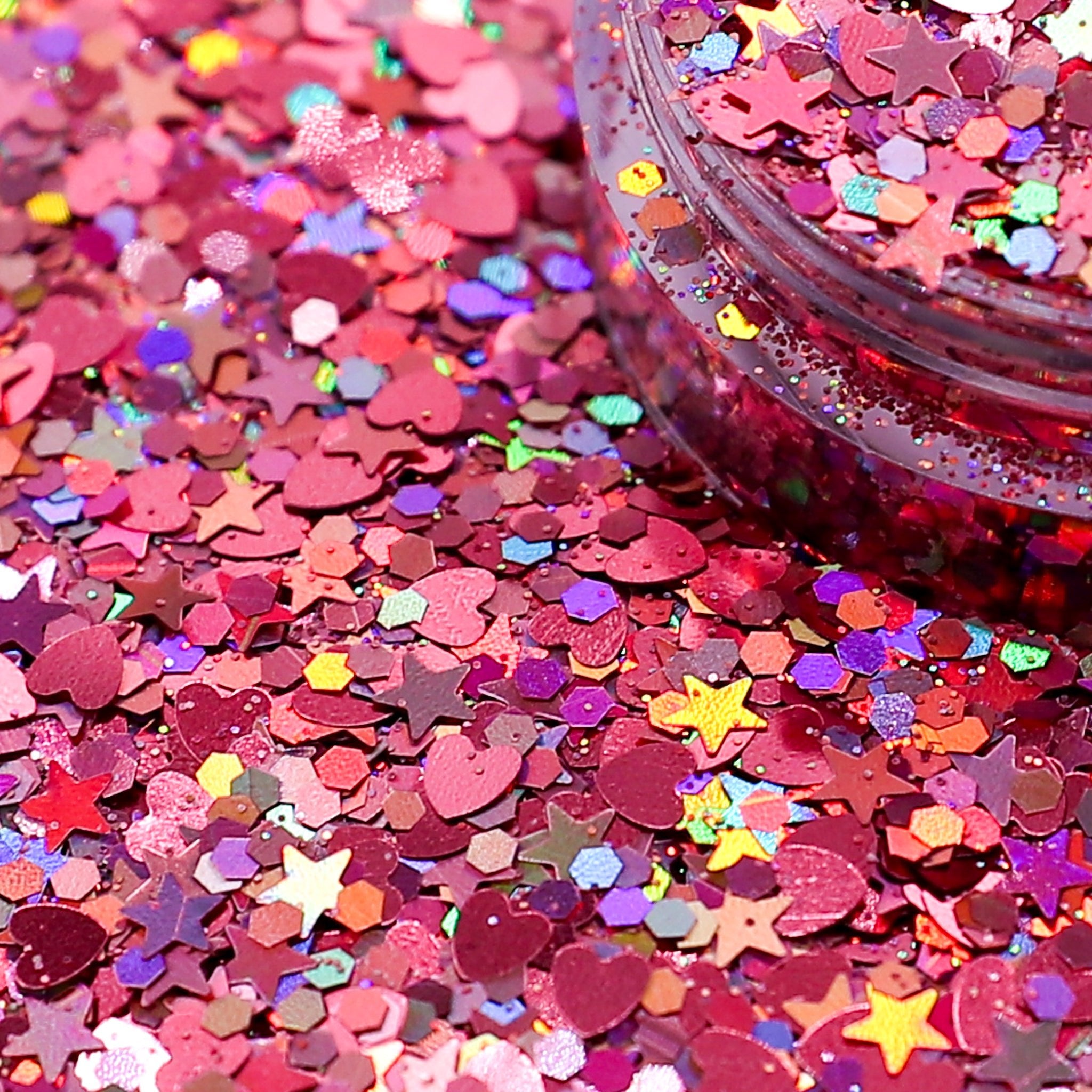 Colorful glitter with star shapes spread out and a container of glitter in the background.