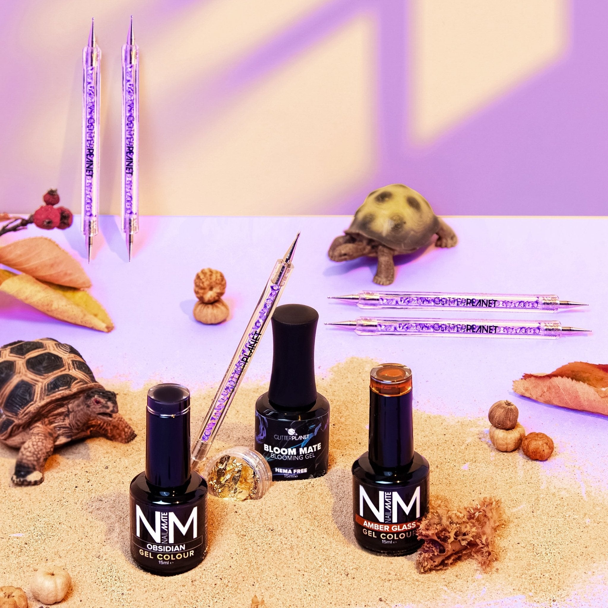 Nail polish bottles with a turtle and decorative elements on a textured sand surface