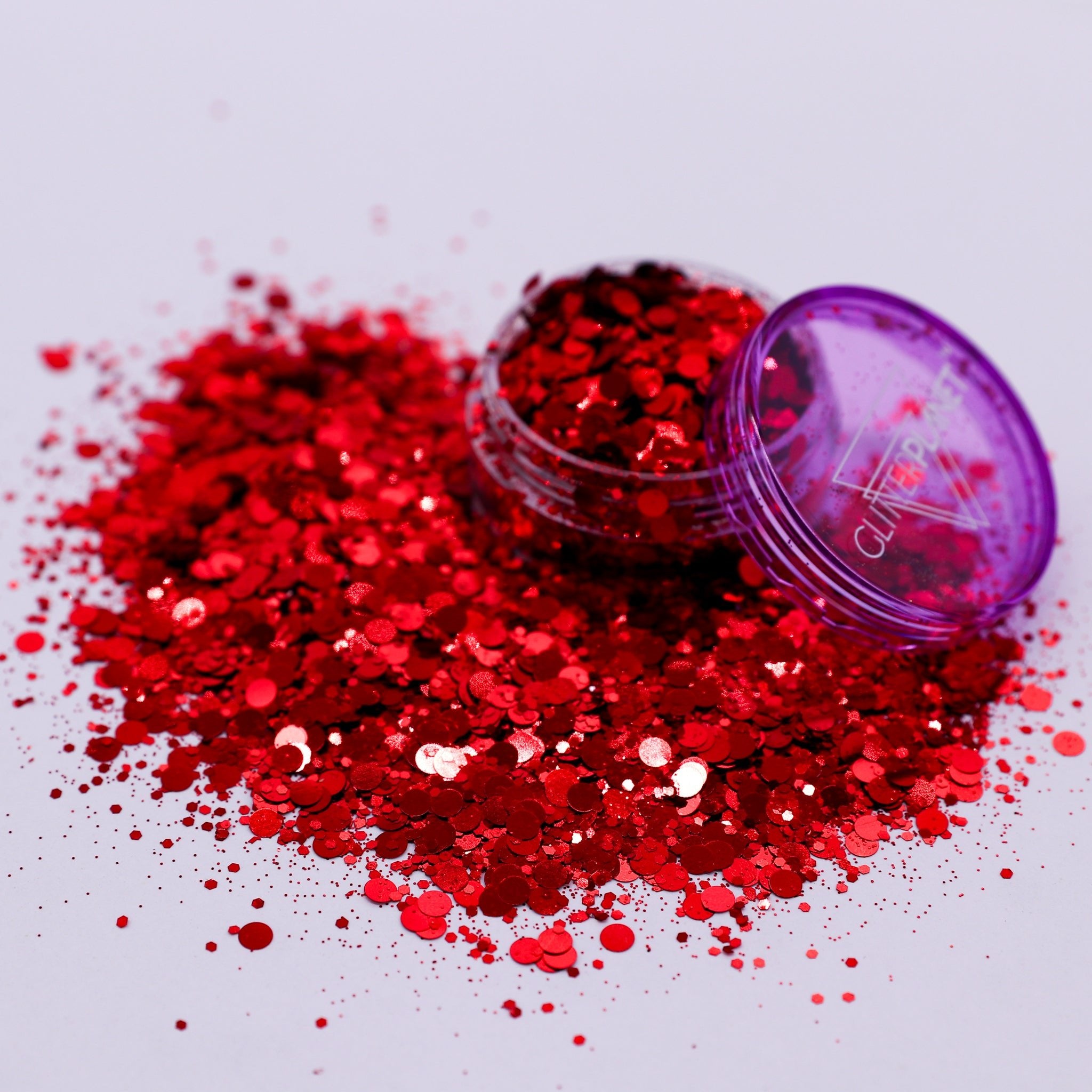 Red glitter spilling out of a purple container on a white background