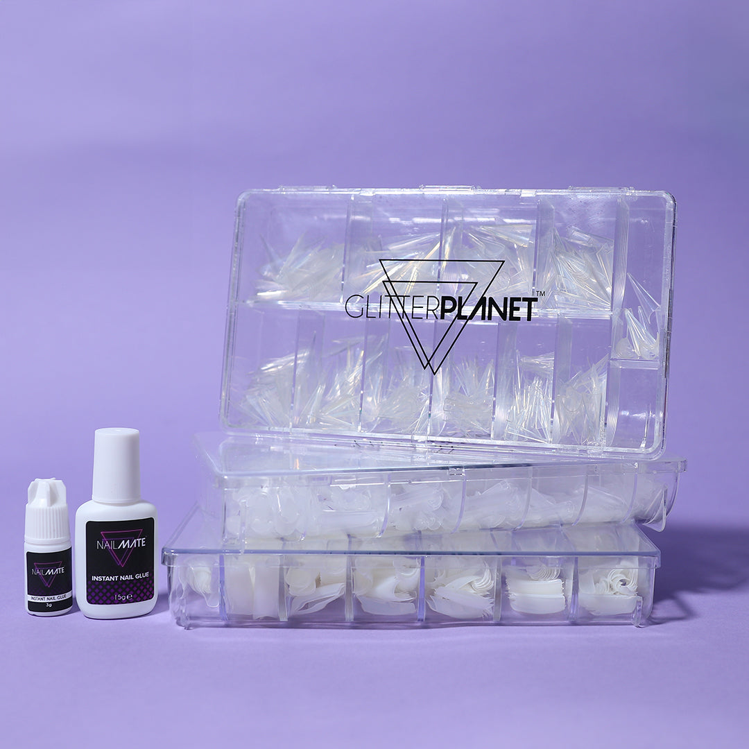 a box of nail tips with some tips out of the box and a gloved hand holding the side on a lilac background