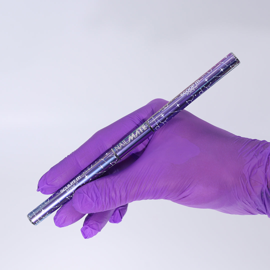 A hand wearing a purple nitrile glove holds a metallic purple and silver nail mate polygel brush against a plain light gray background.