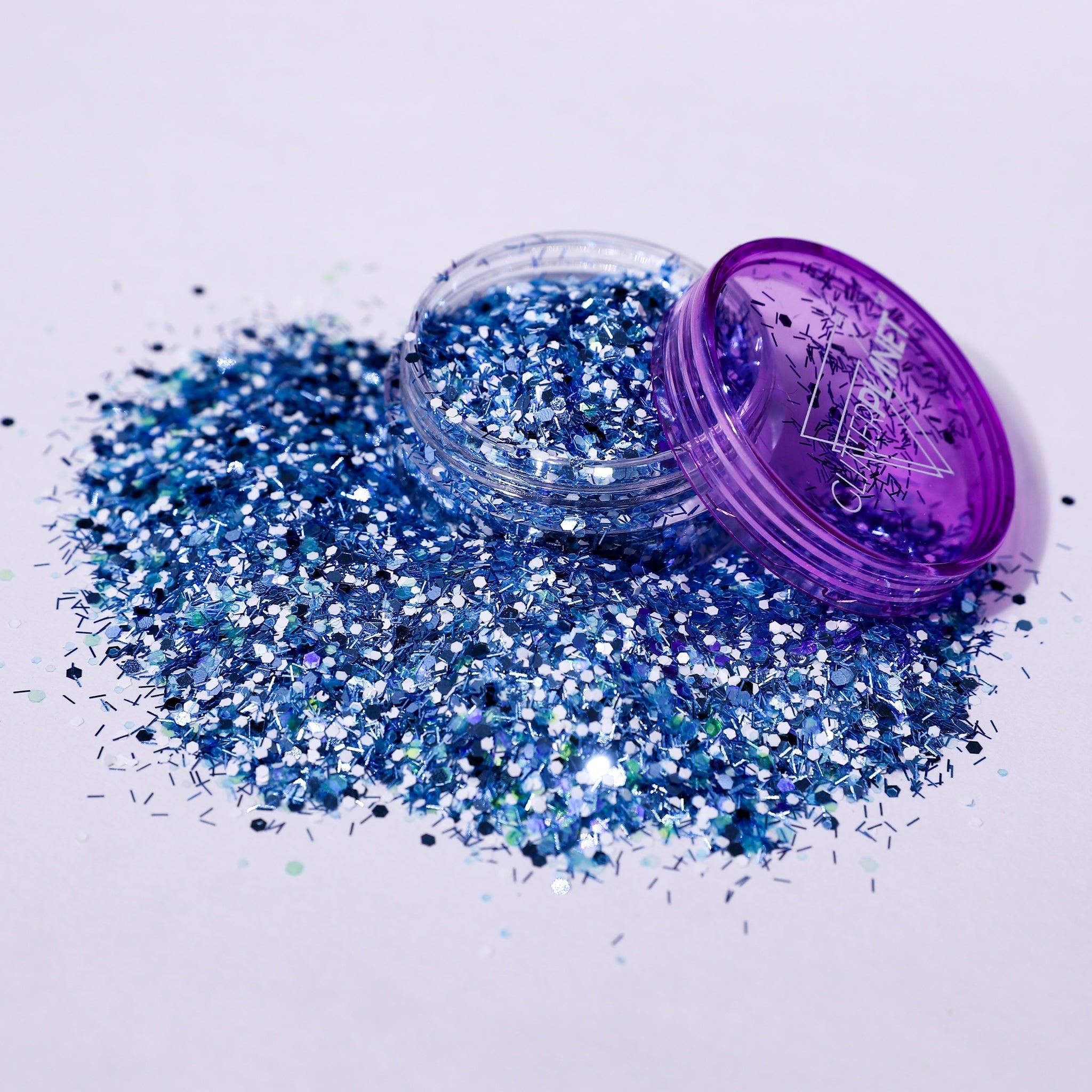 Blue glitter spilling out of a purple container on a white background