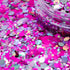 Colorful glitter with a clear container on a pink background