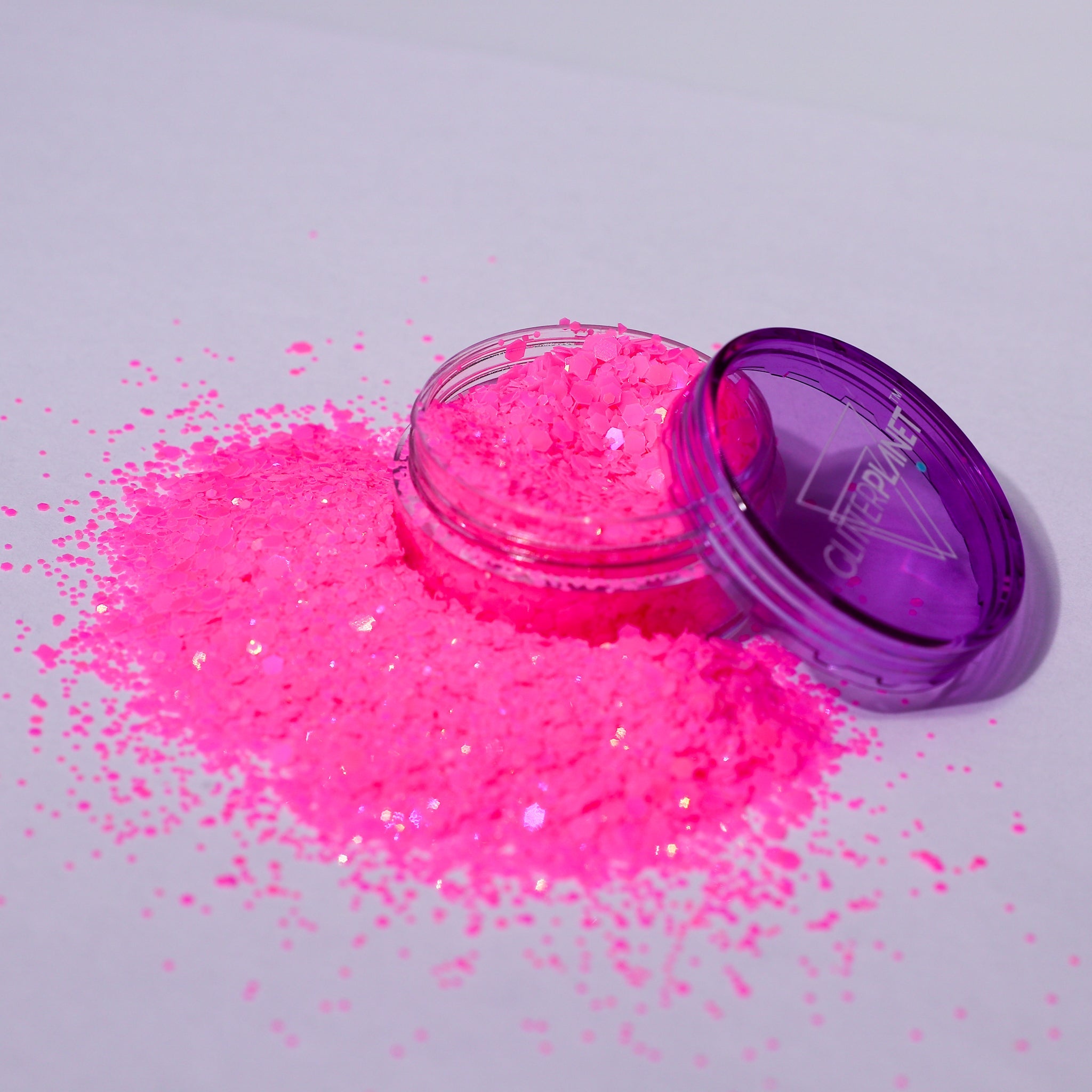 Open container of pink glitter with spilled glitter on a light gray background