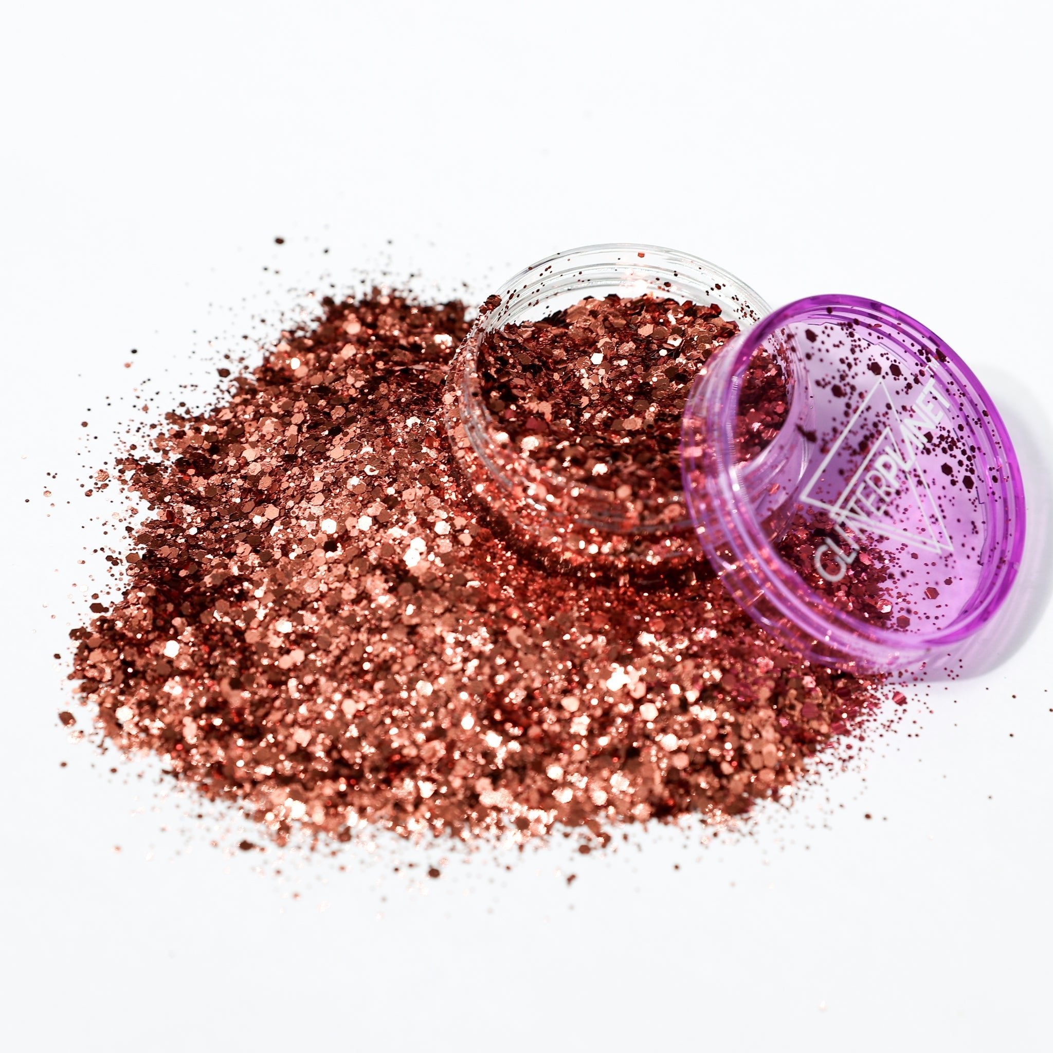Bronze glitter spilling out of a purple container on a white background