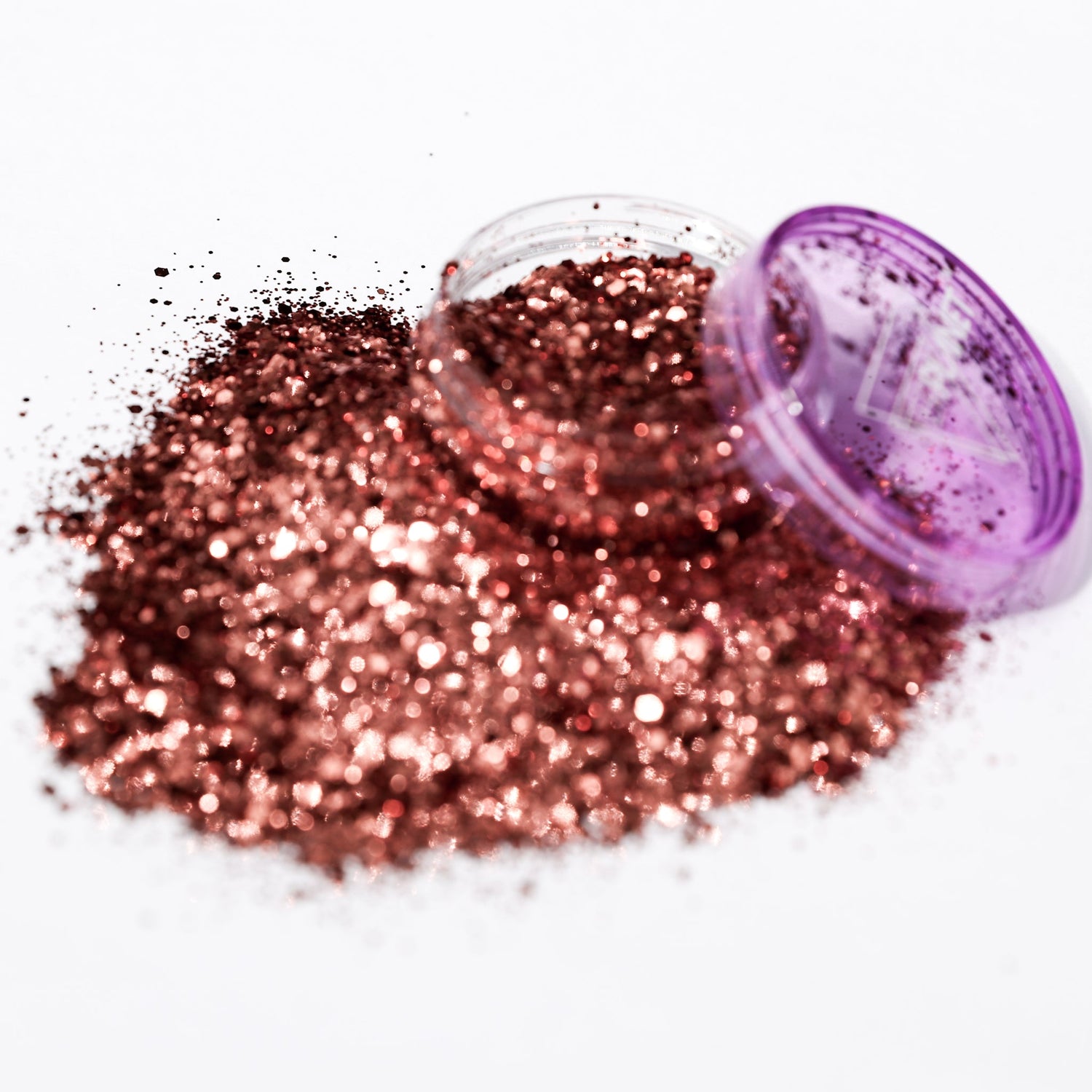 Bronze glitter spilling out of a purple container on a white background