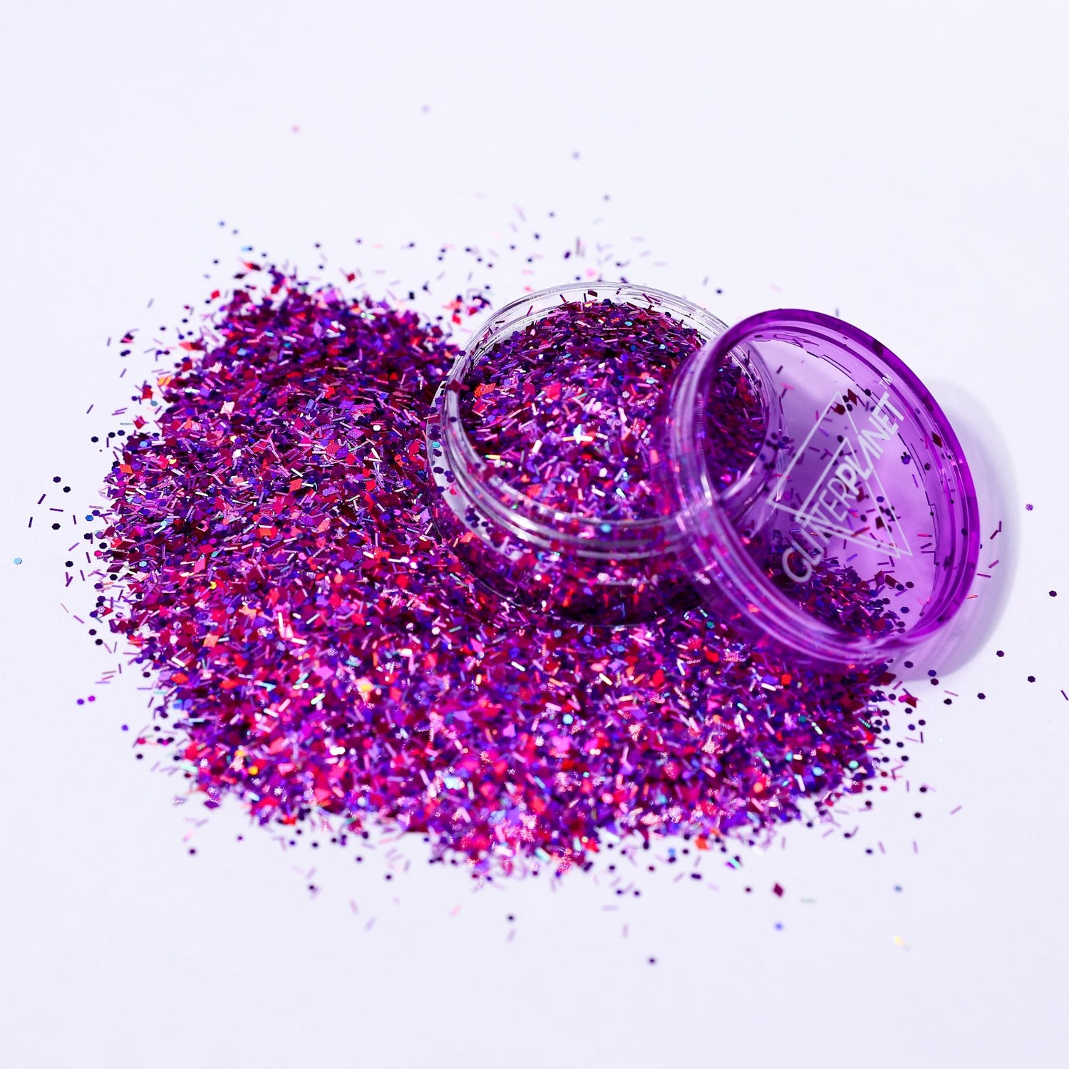 Purple glitter spilling out of a small open container on a white background