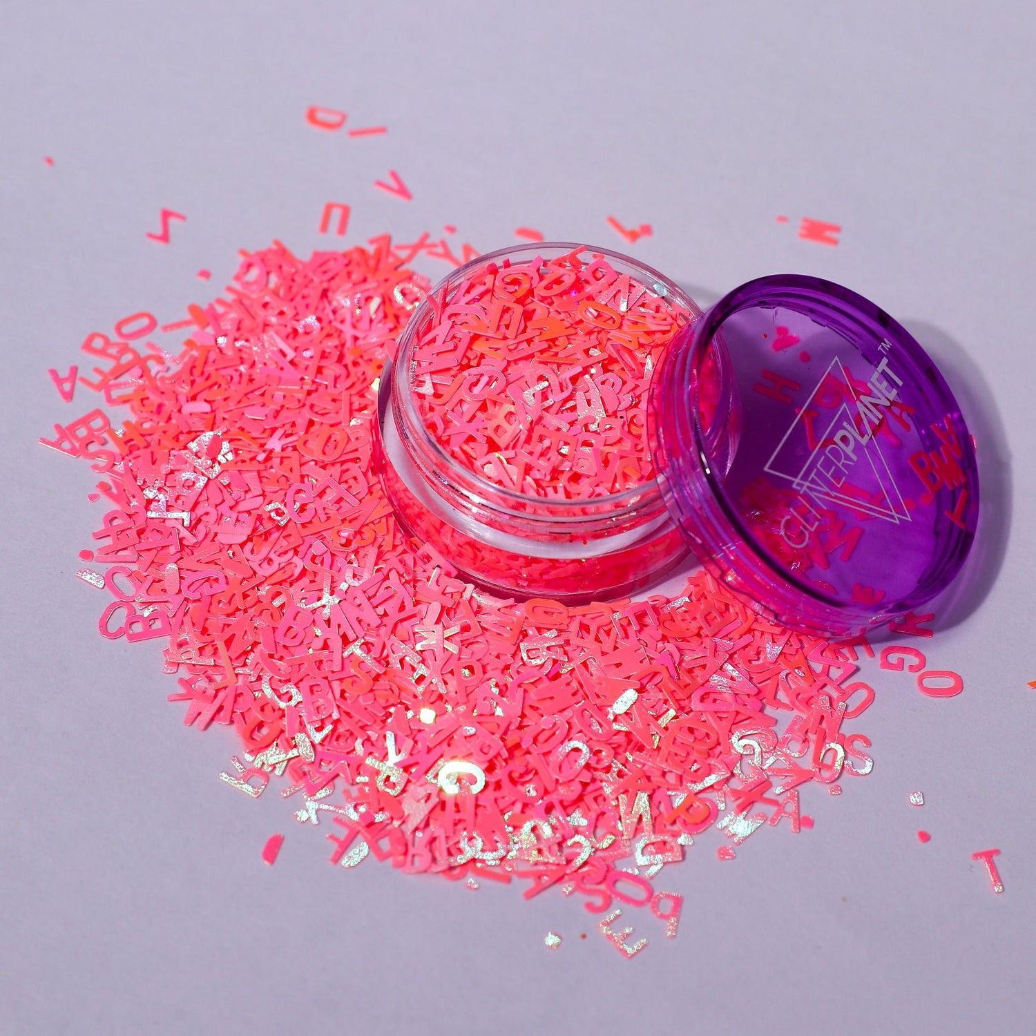 coral letter-shaped confetti spilling out of a container on a gray background