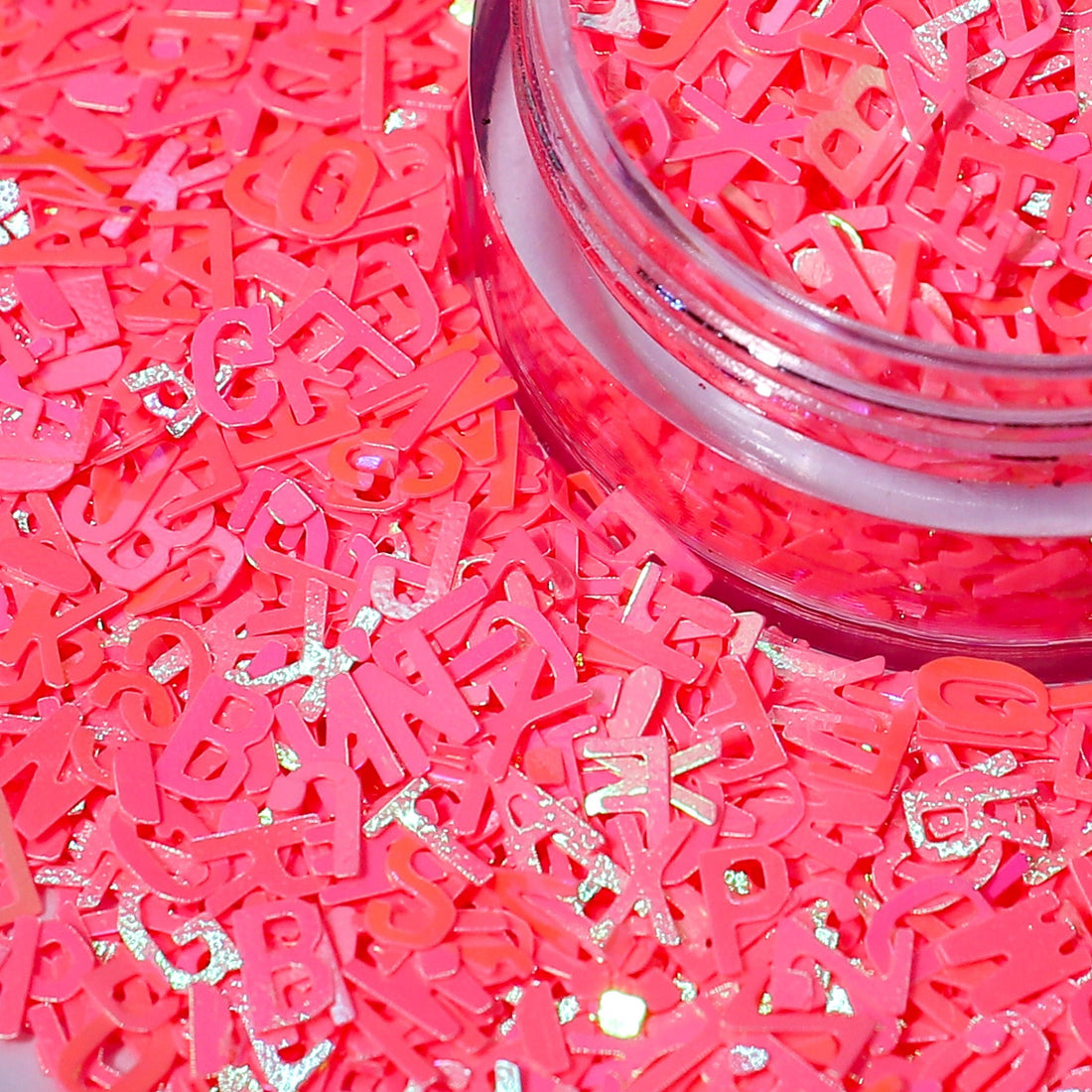 coral letter-shaped confetti with glitter in a clear container.