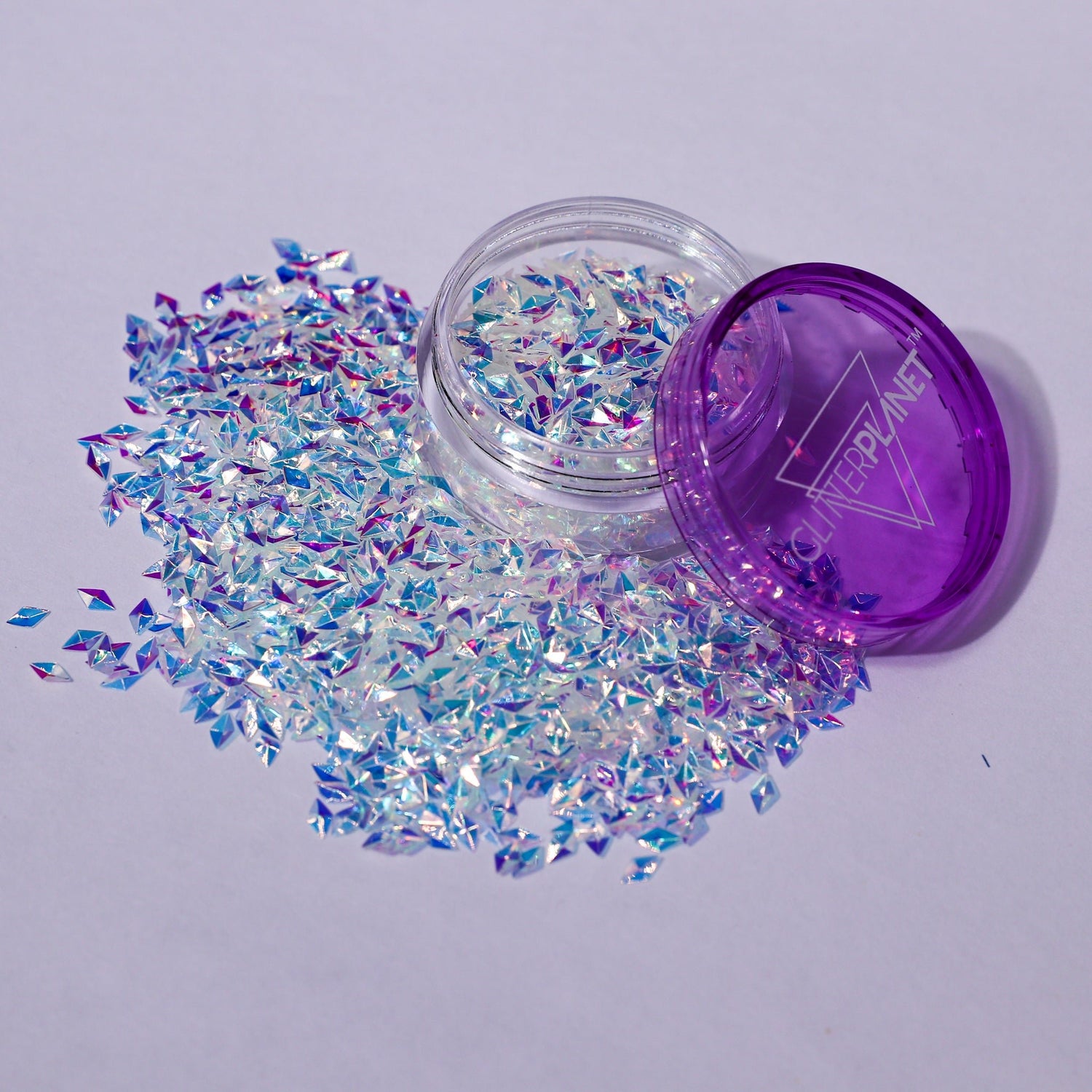 Iridescent glitter spilling out of a purple container on a light gray background