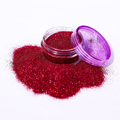 Red glitter in an open clear container with a purple lid on a white background