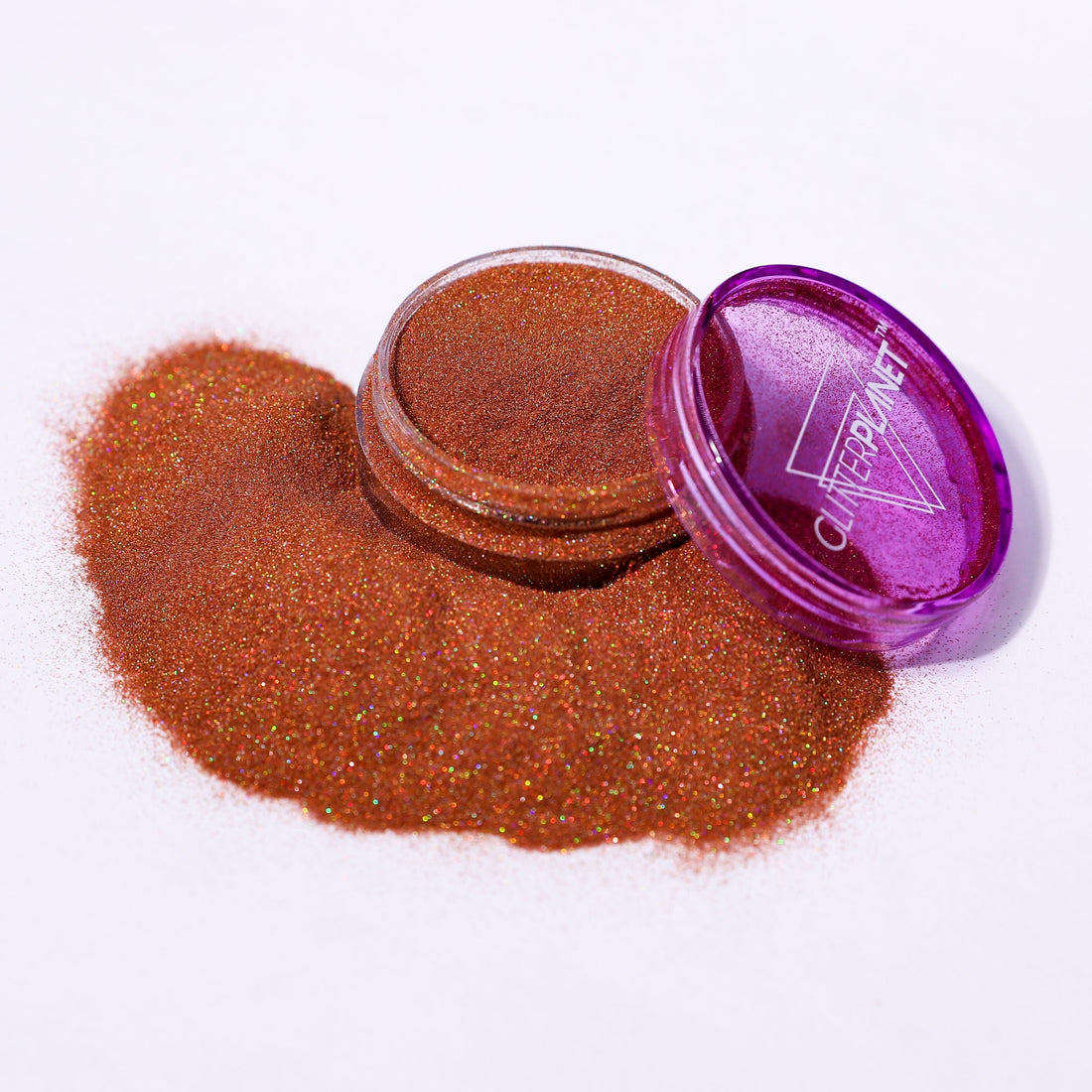 Open purple container of glitter with spilled glitter on a white background
