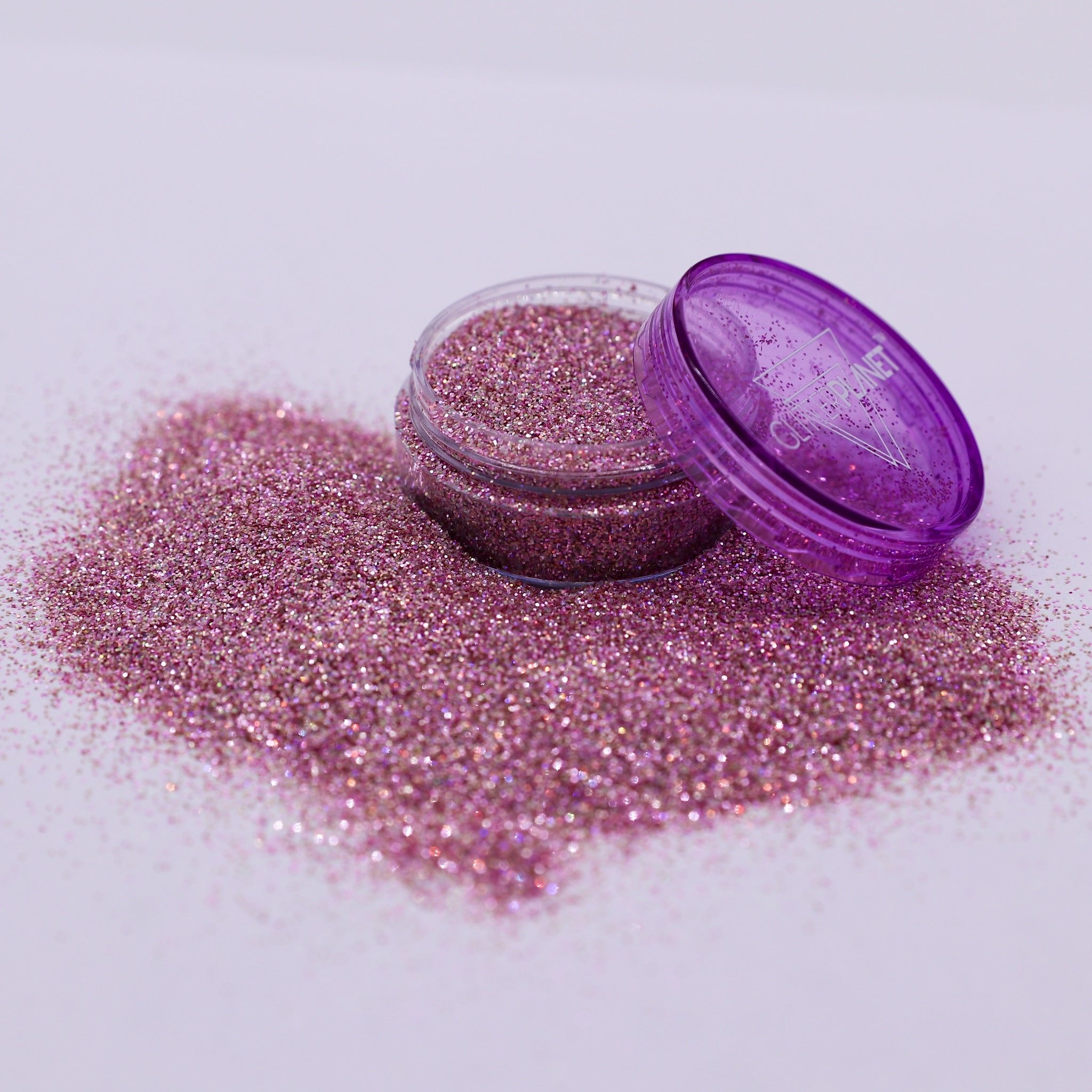 Pink glitter in an open container with a purple lid on a white background