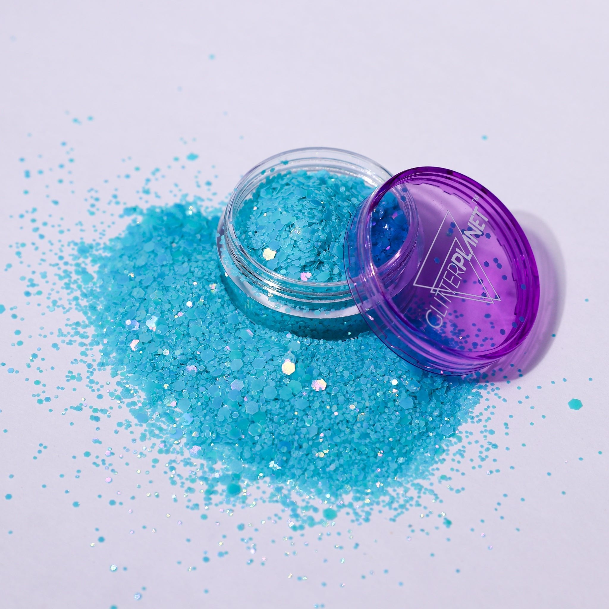 Open container of blue glitter with a purple lid on a white background
