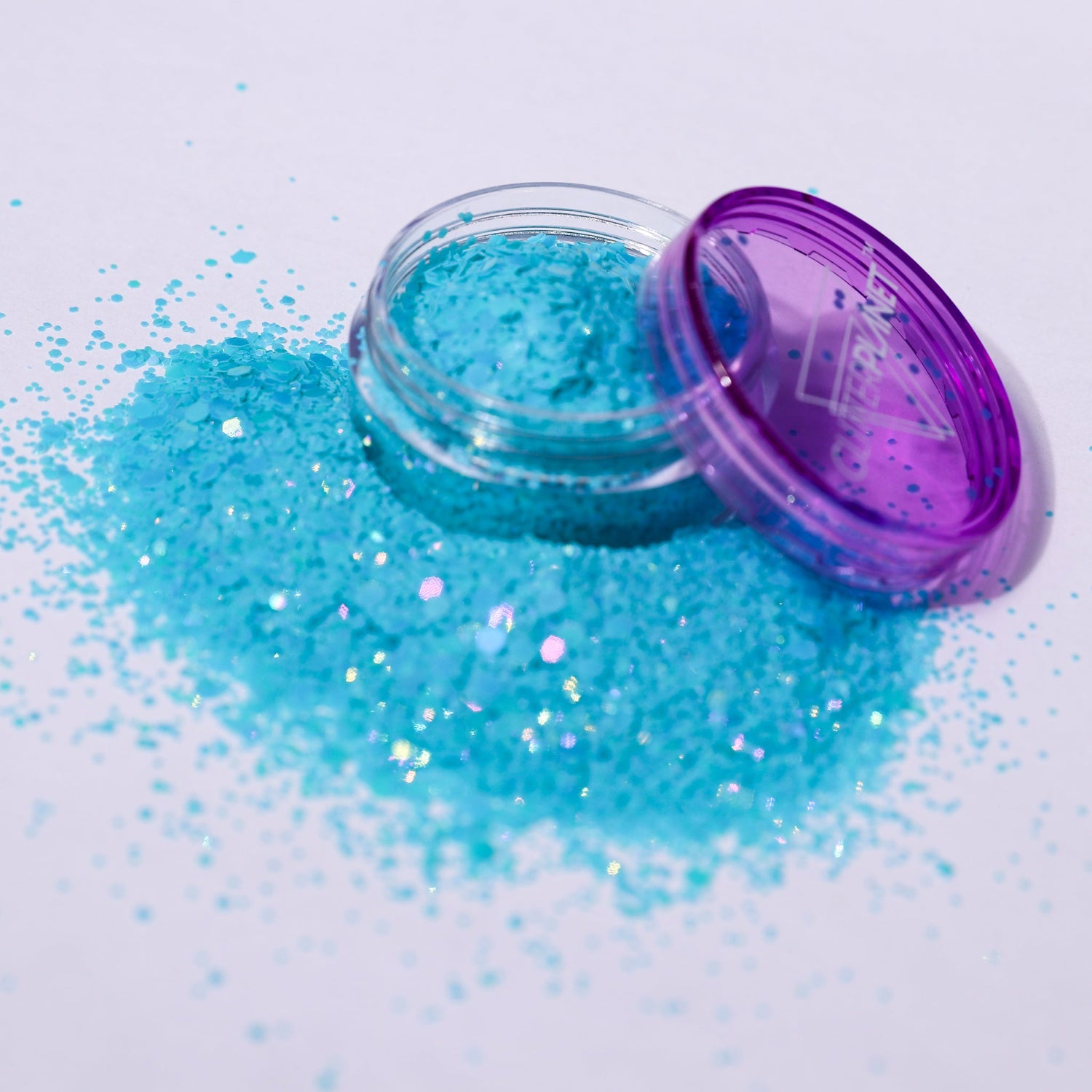 Open container of blue glitter with spilled glitter on a white background