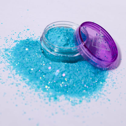 Open container of blue glitter with spilled glitter on a white background
