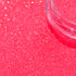 Close-up of pink glitter with a clear container on a pink background