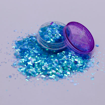 Blue glitter spilling out of a small open container with a purple lid on a light gray background.