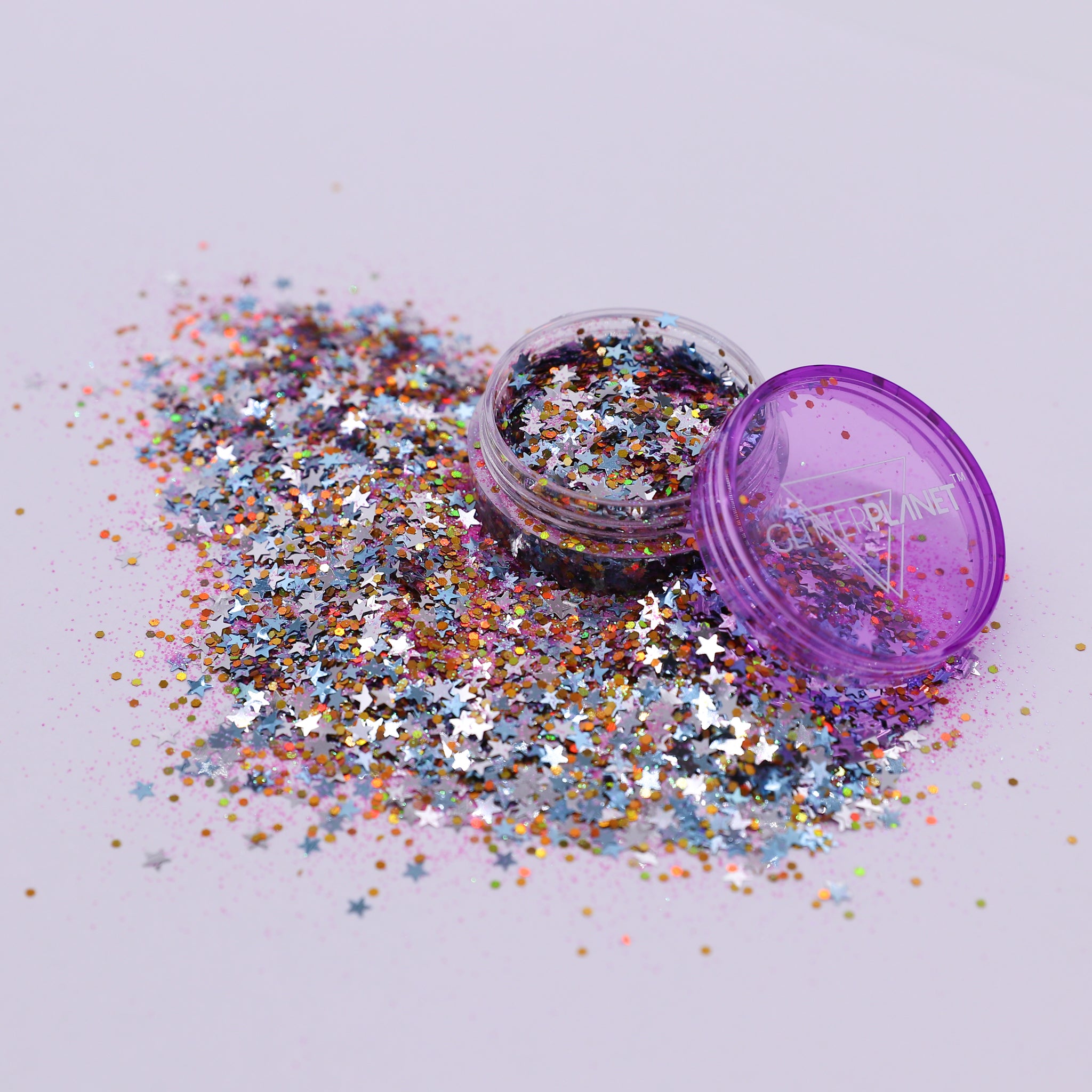 Multicolored glitter spilling out of a purple container on a light gray background