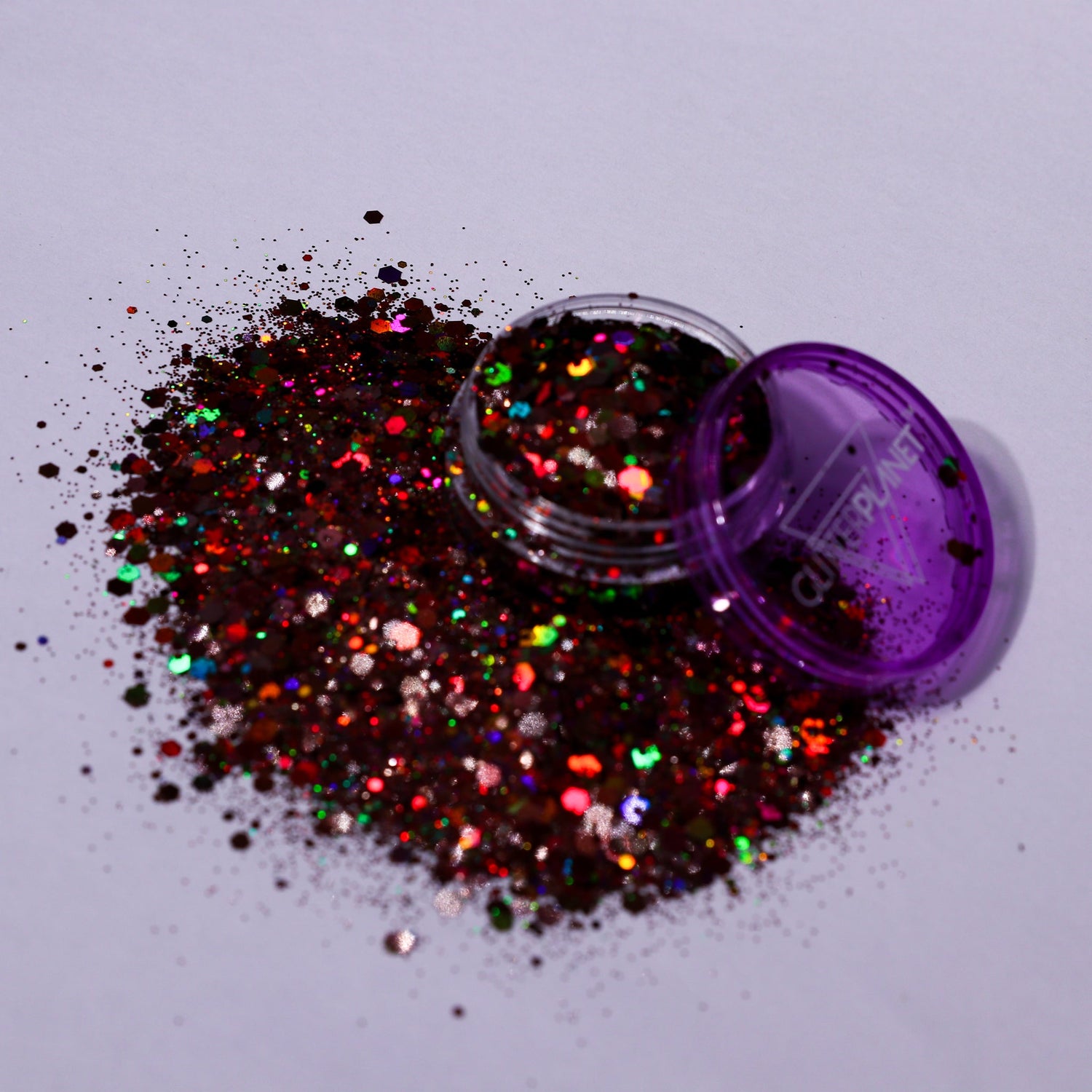 Multicolored glitter spilling out of a purple container on a light gray background