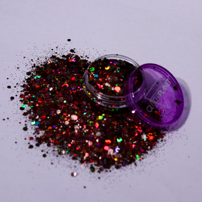 Multicolored glitter spilling out of a purple container on a light gray background