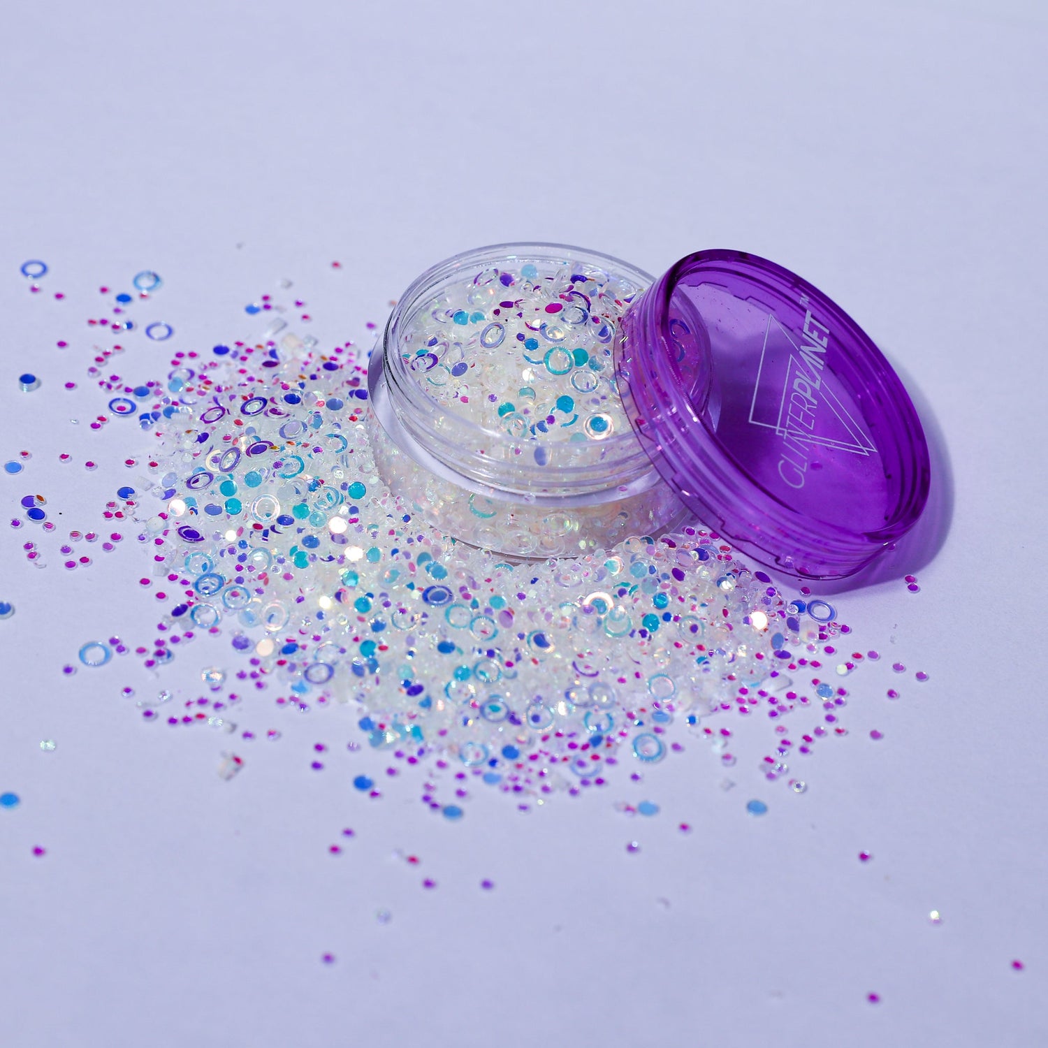 Open jar of glitter with scattered glitter on a light purple background