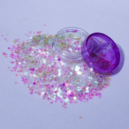 Star-shaped glitter spilling out of a clear container with a purple lid on a light purple background.