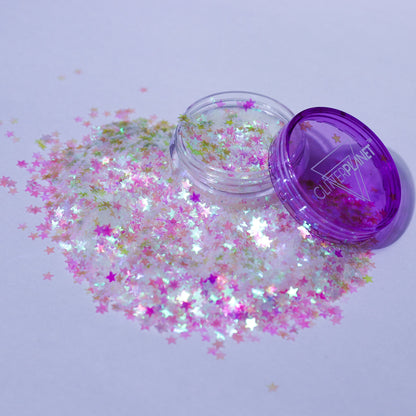 Clear container of star-shaped glitter with a purple lid on a light gray background