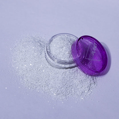 Small open container of glitter with a purple lid on a light gray background