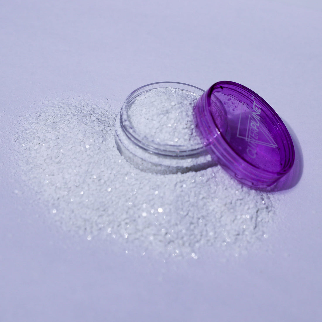 Open container of glitter with purple lid on a light purple background