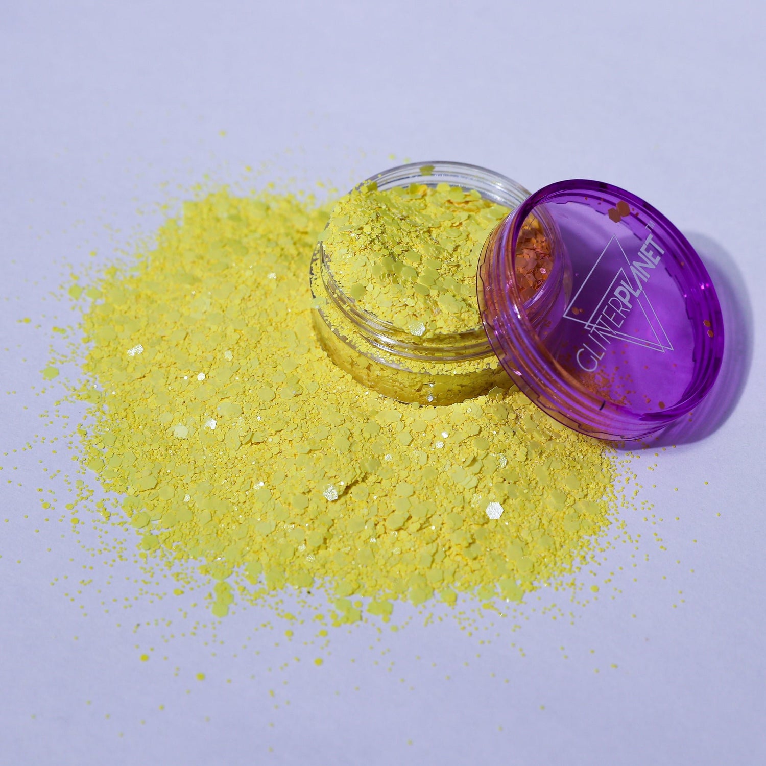 Clear container with purple lid on a white background, filled with yellow glitter.