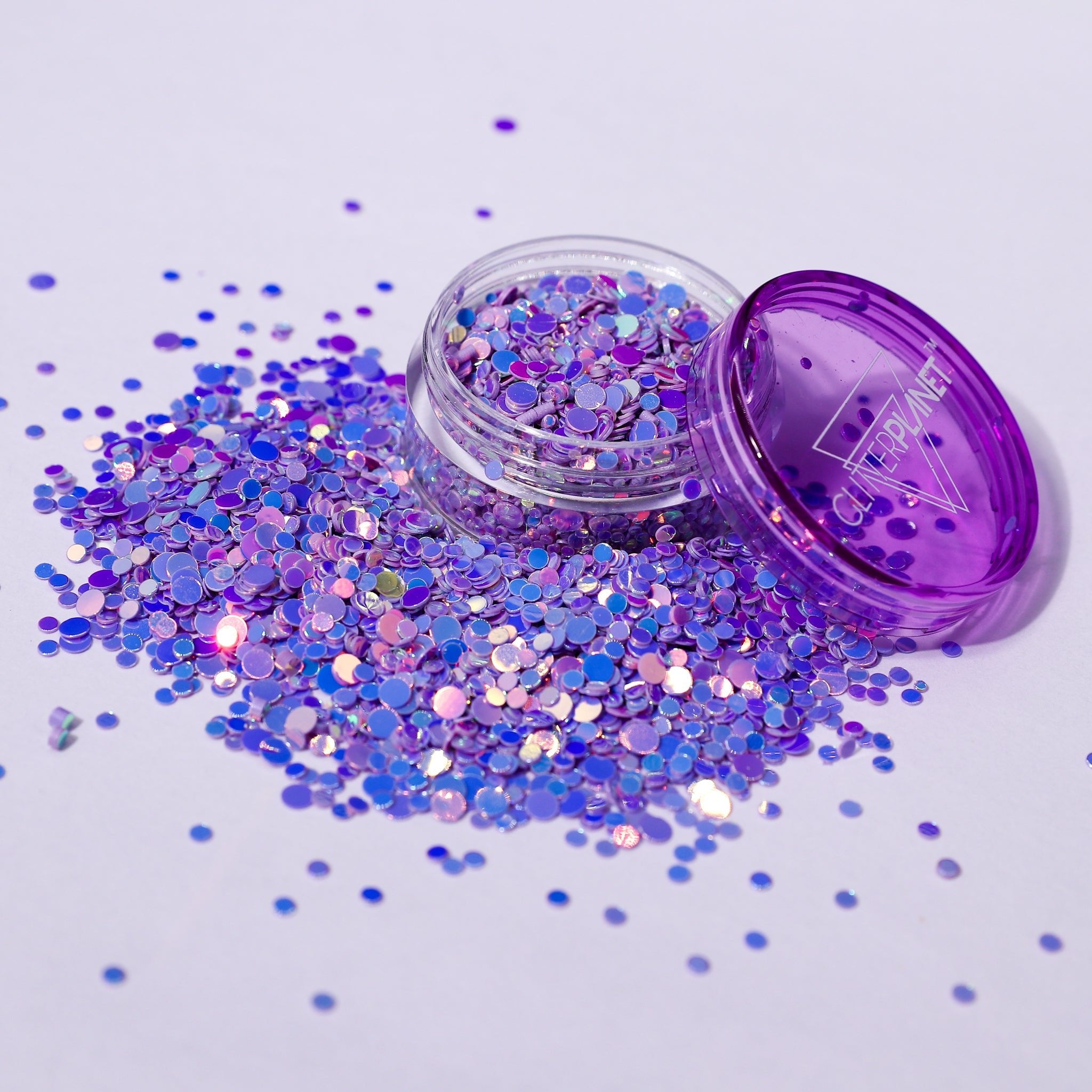 Open container of purple glitter with scattered glitter on a light purple background