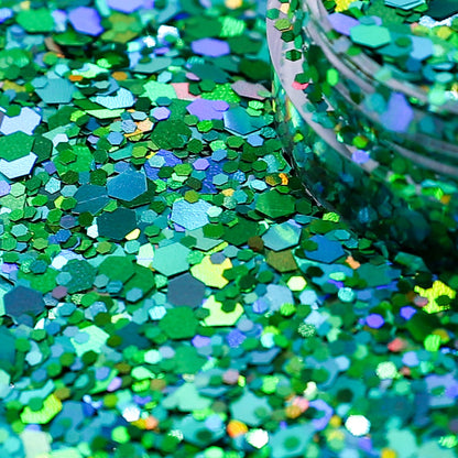 Close-up of green glitter with a jar partially filled with glitter in the background.