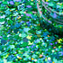 Close-up of green glitter with a jar partially filled with glitter in the background.