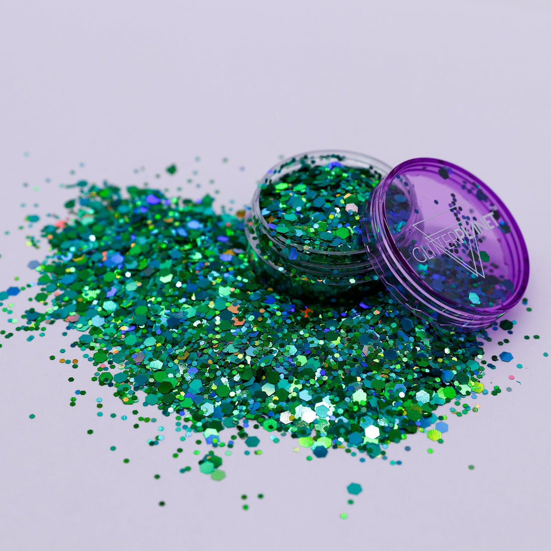 Green glitter spilling out of a purple container on a light gray background